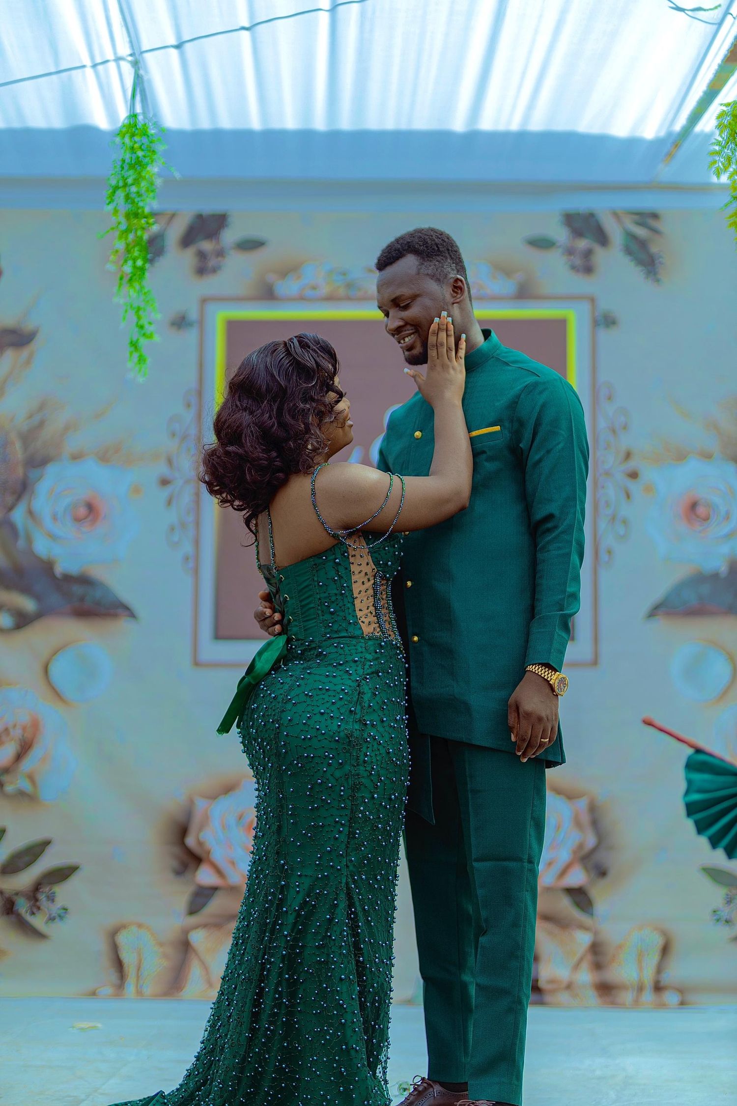 Couple in matching emerald green formal wear share intimate moment against floral backdrop.