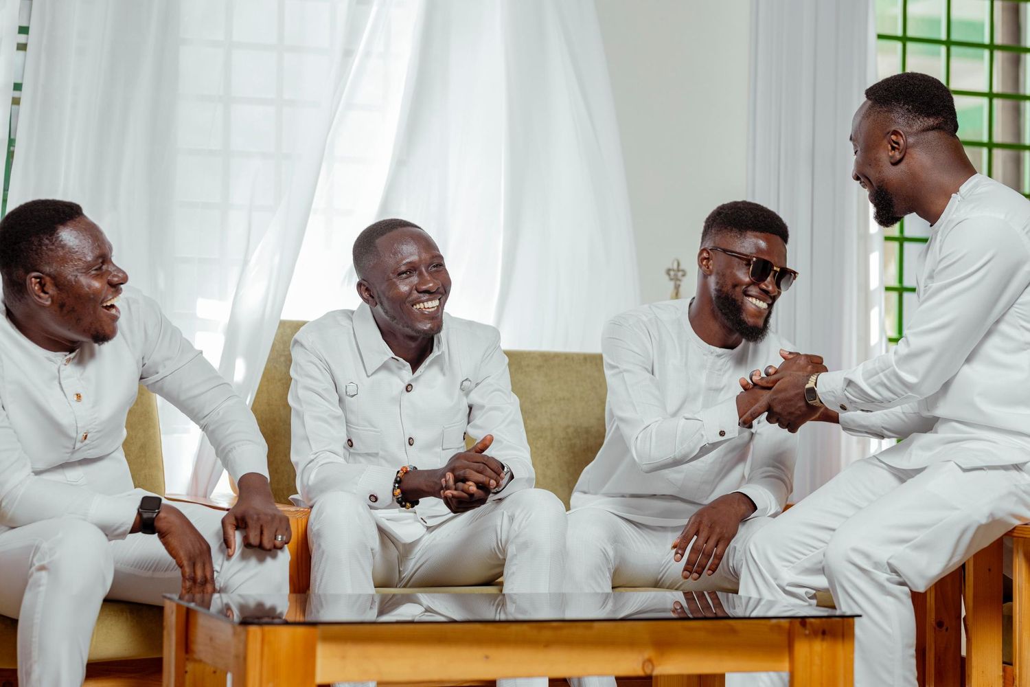 Four people in crisp white outfits share a casual moment on wooden bench.