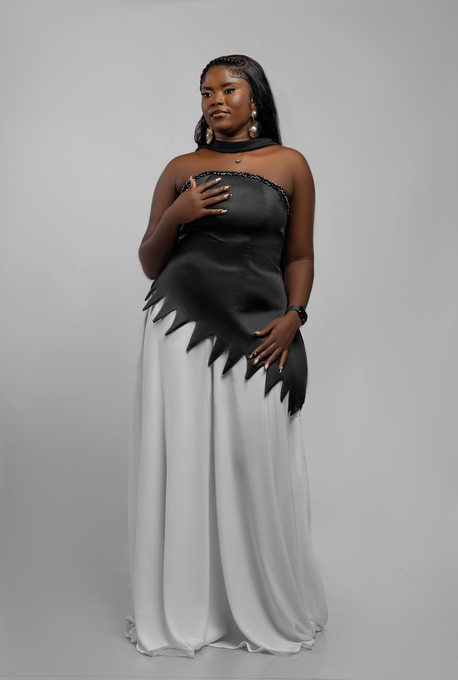 A model wearing a striking black and white gown poses gracefully against a gray studio backdrop in a fashion photoshoot series.