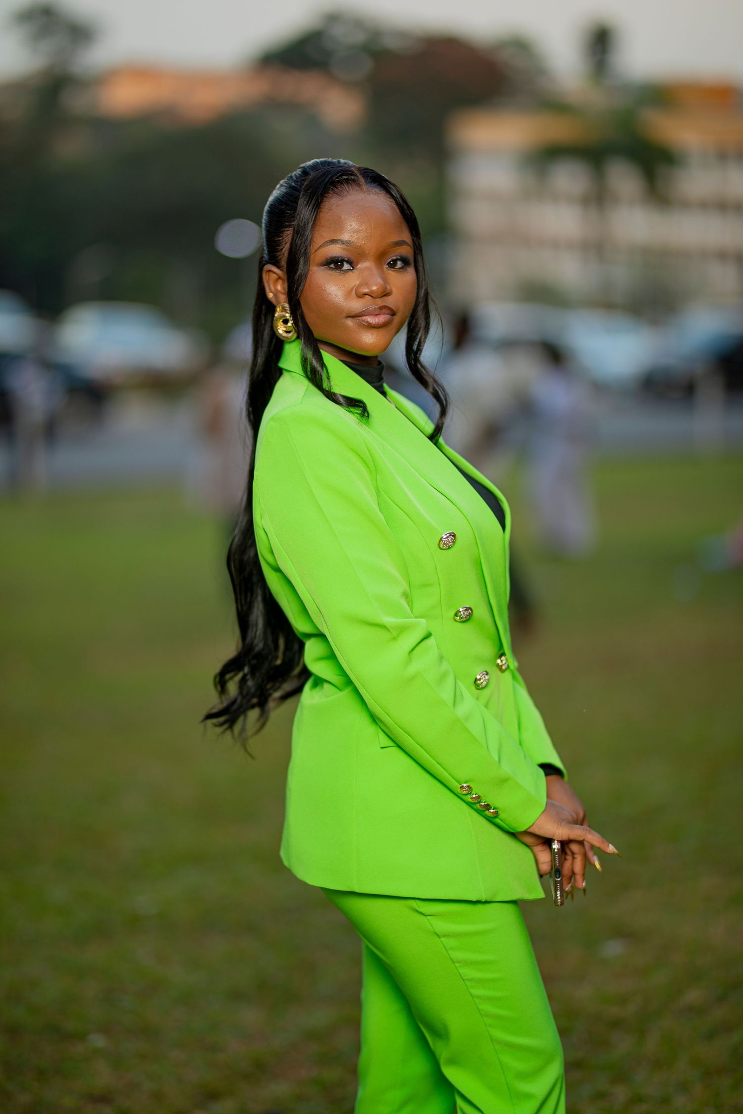 A person poses outdoors wearing a vibrant neon green business suit in a grassy field.