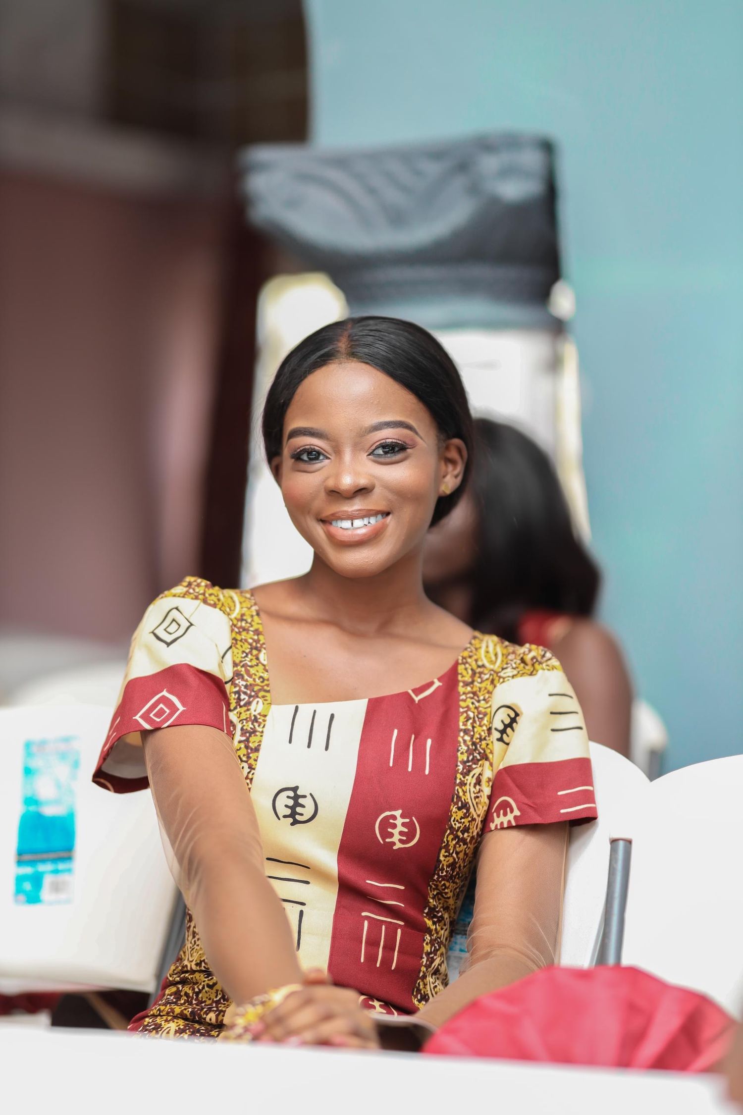 Woman in traditional red and gold patterned dress sits at event.