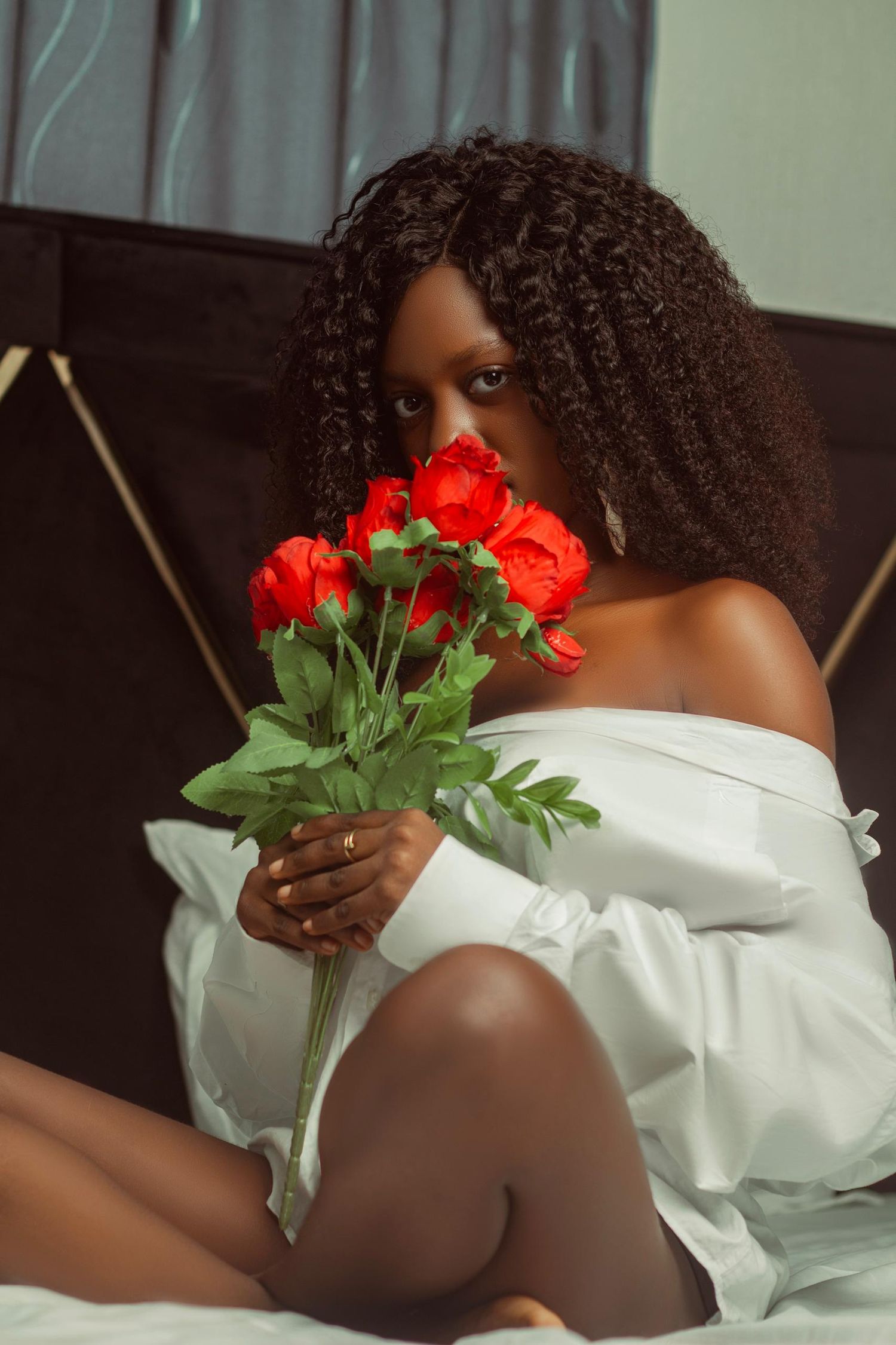 Artistic boudoir photo with model in white dress holding red roses.