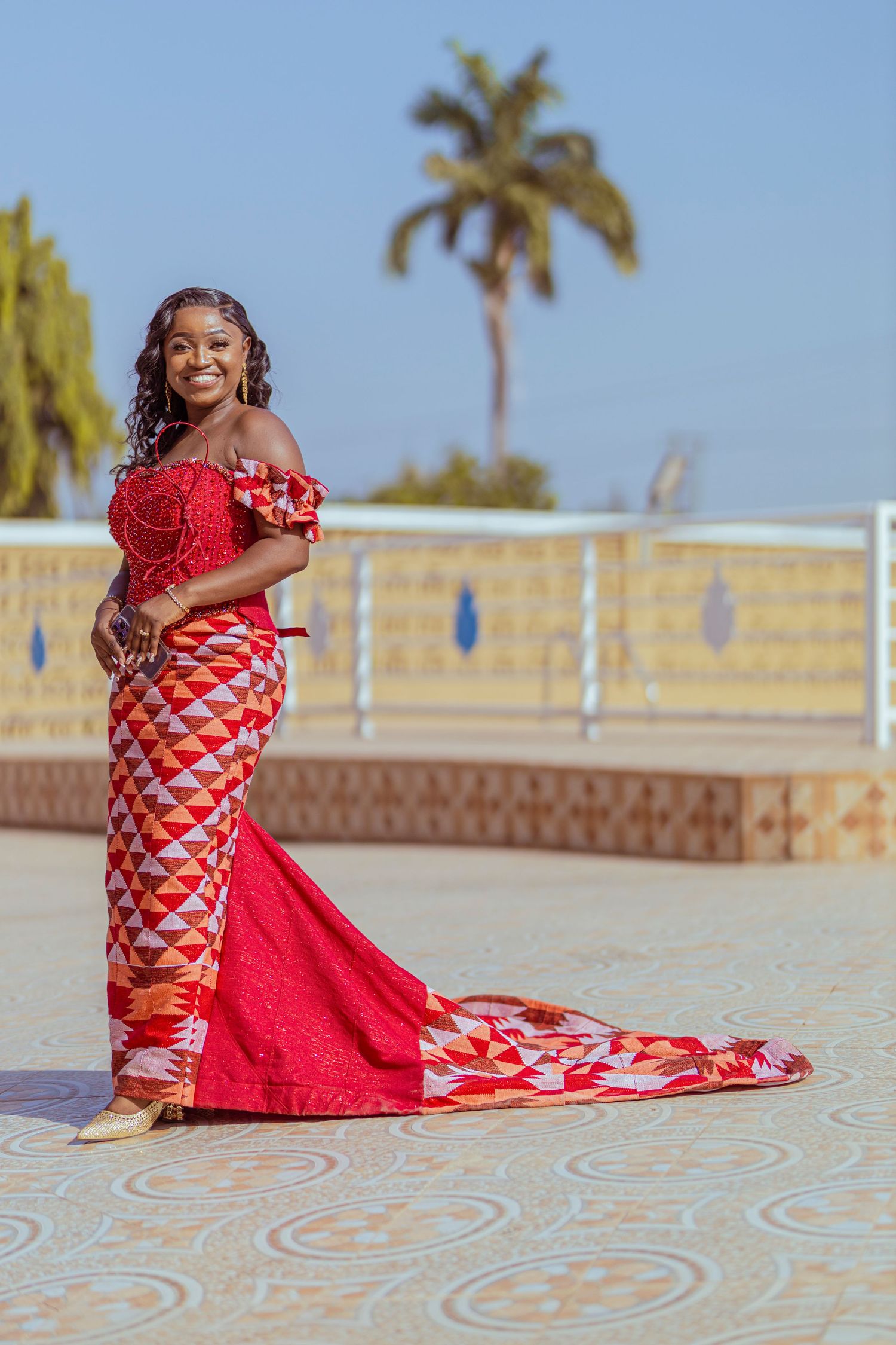 Red and white patterned formal dress with a flowing train against a palm tree backdrop.