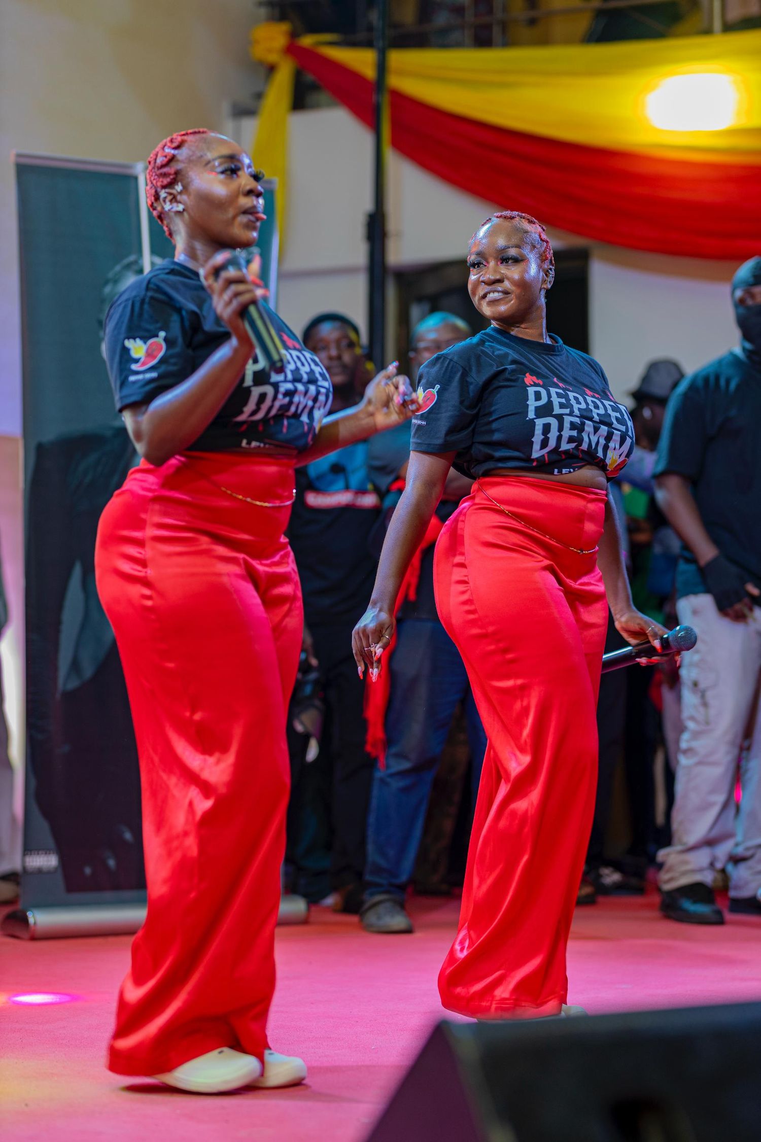 Two performers in matching red pants and black shirts dancing on a pink-lit stage.