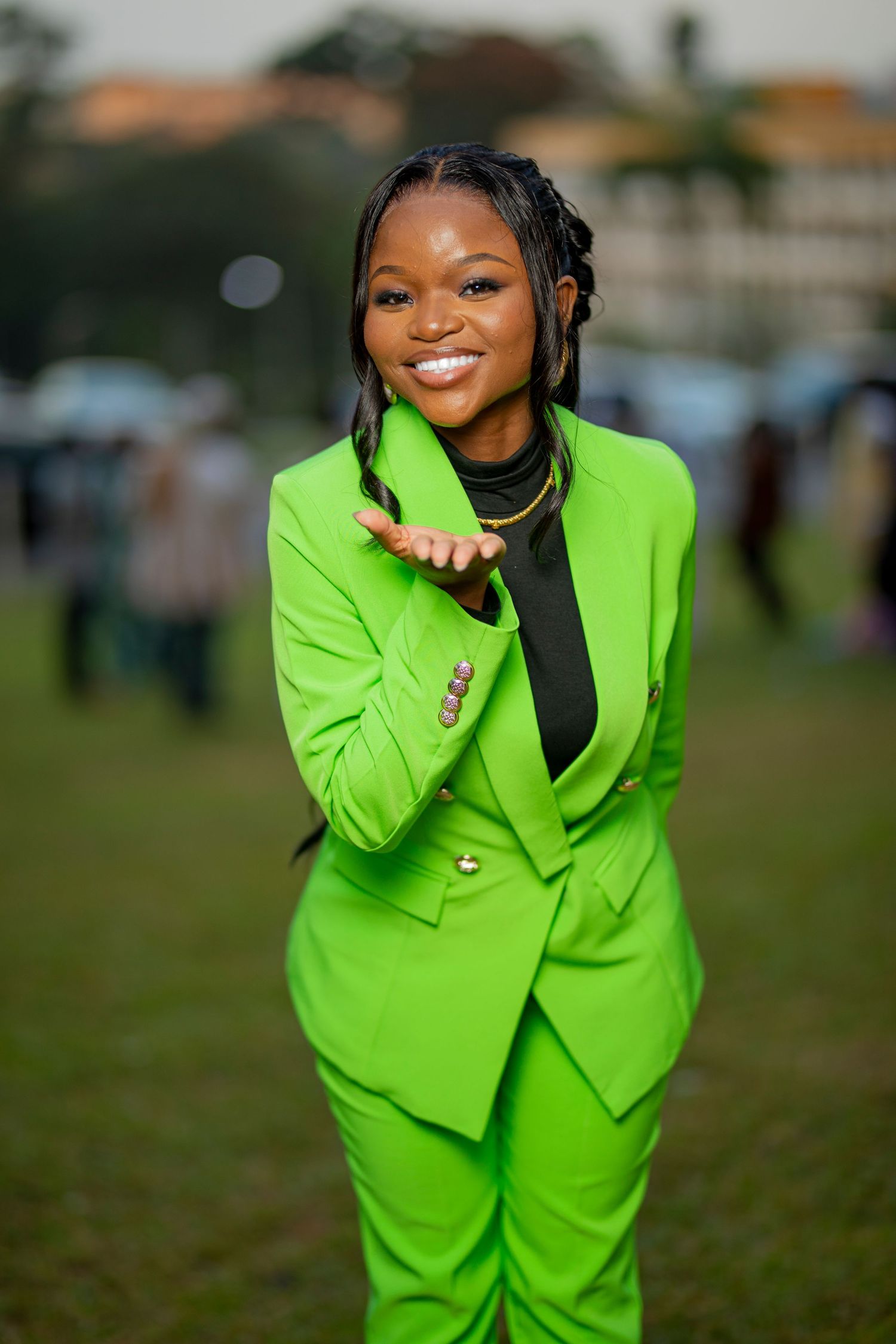 A person wearing a vibrant lime green business suit poses playfully outdoors on grass against a blurred background.