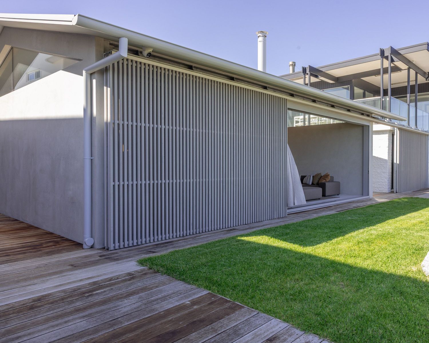 Minimalist exterior with vertical metal cladding and wooden deck overlooking green lawn.
