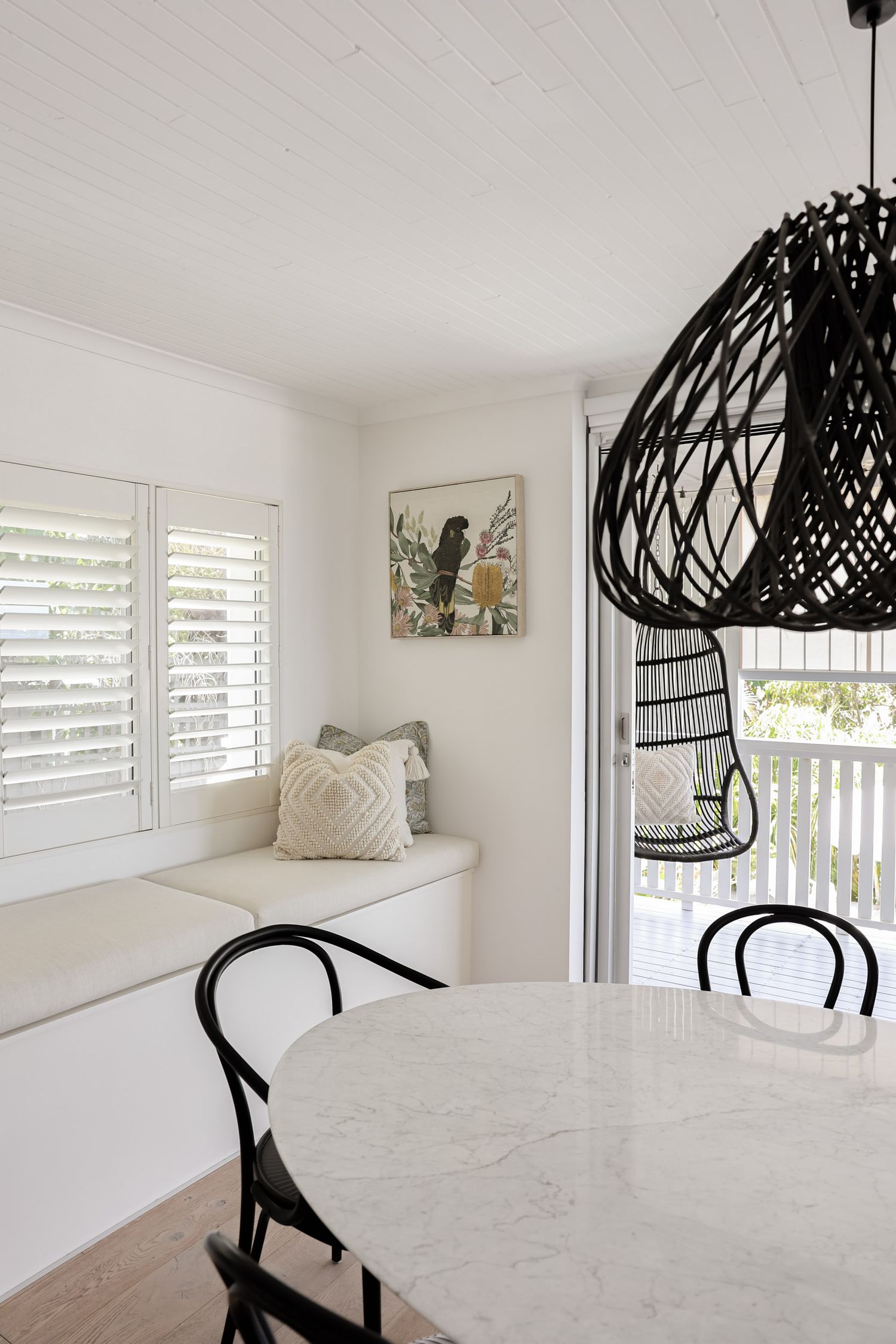 Bright dining space with marble table, black bentwood chairs, and dramatic woven pendant light.