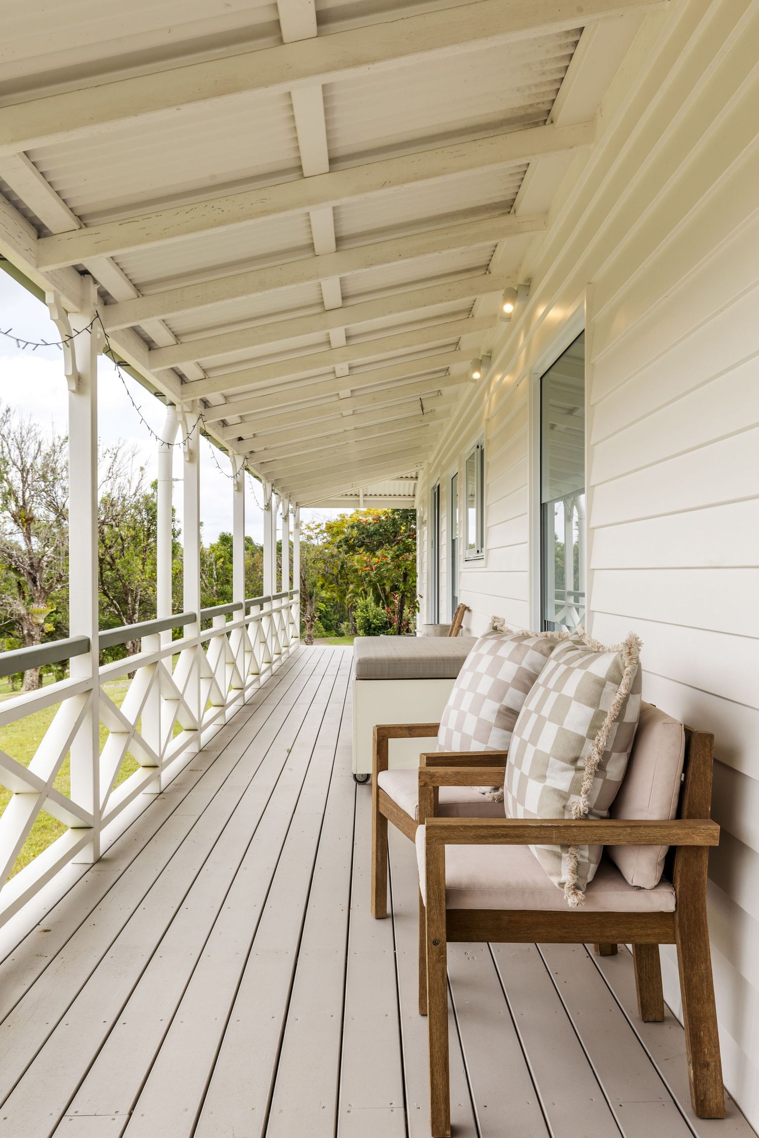 Cozy wooden chairs with plush cushions on a white painted wraparound porch with diagonal railing details.