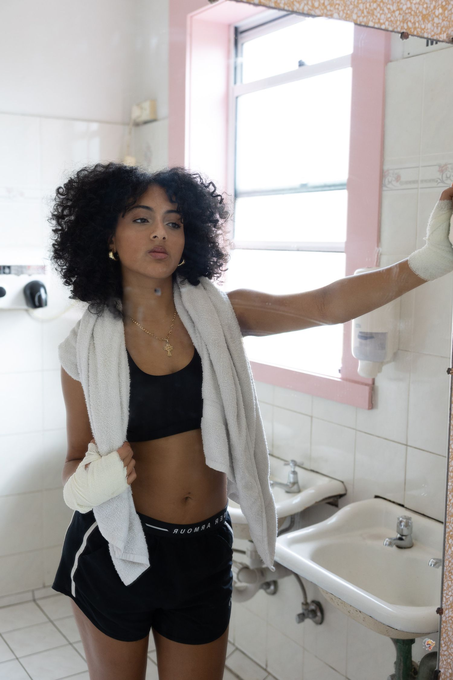 Athletic woman in workout attire posing in bathroom with natural lighting.