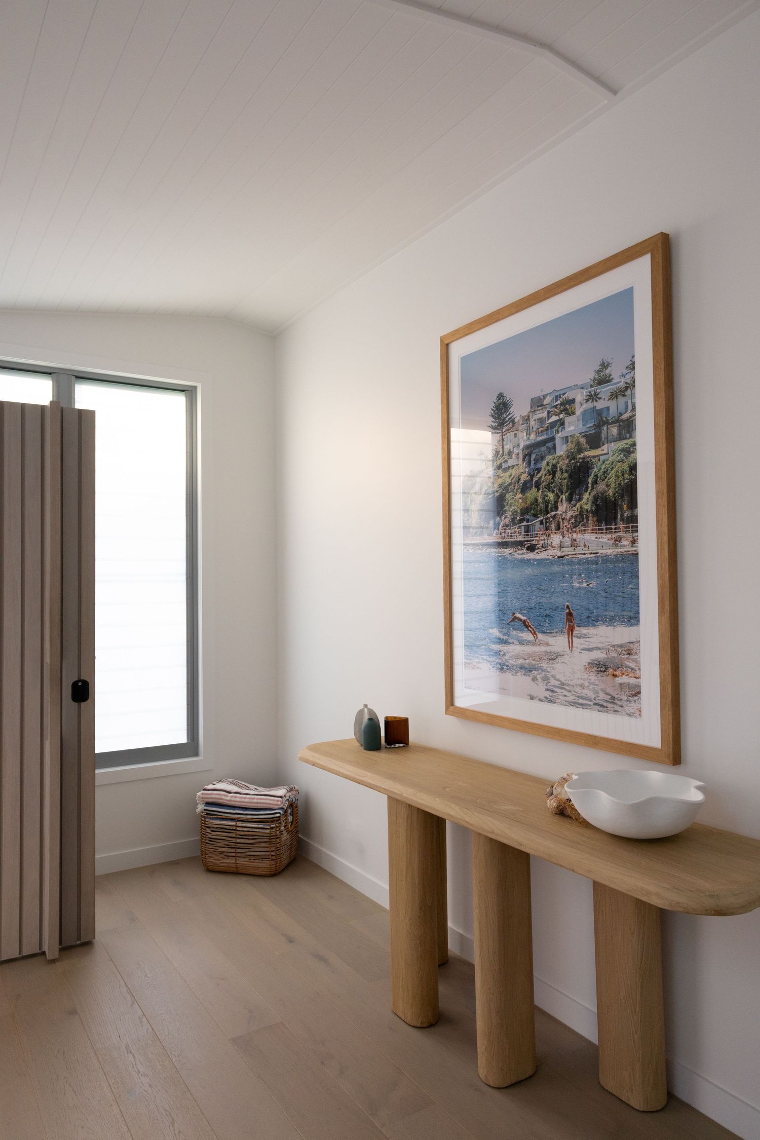 A series of five minimalist interior photos showing a white room with wooden console tables and coastal artwork on the walls.