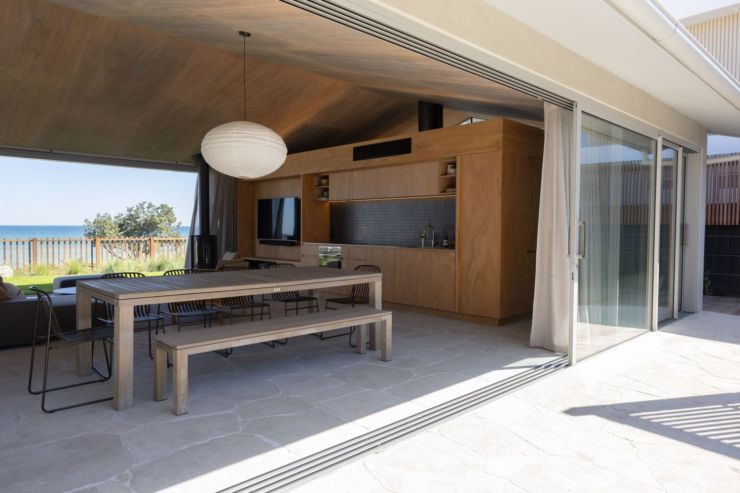 Beachfront dining area with long wooden table and bench seating overlooking the ocean.