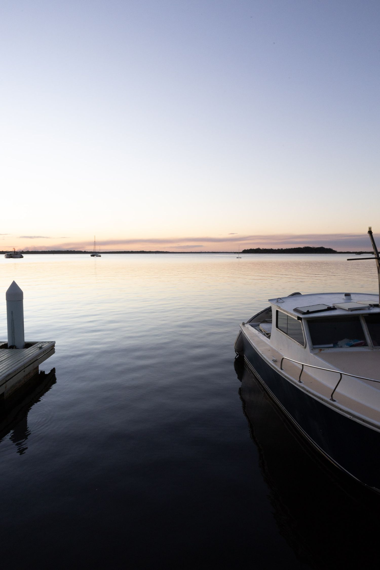 Serene harbor view at dusk with moored boat and wooden pier post silhouetted against pastel sky.