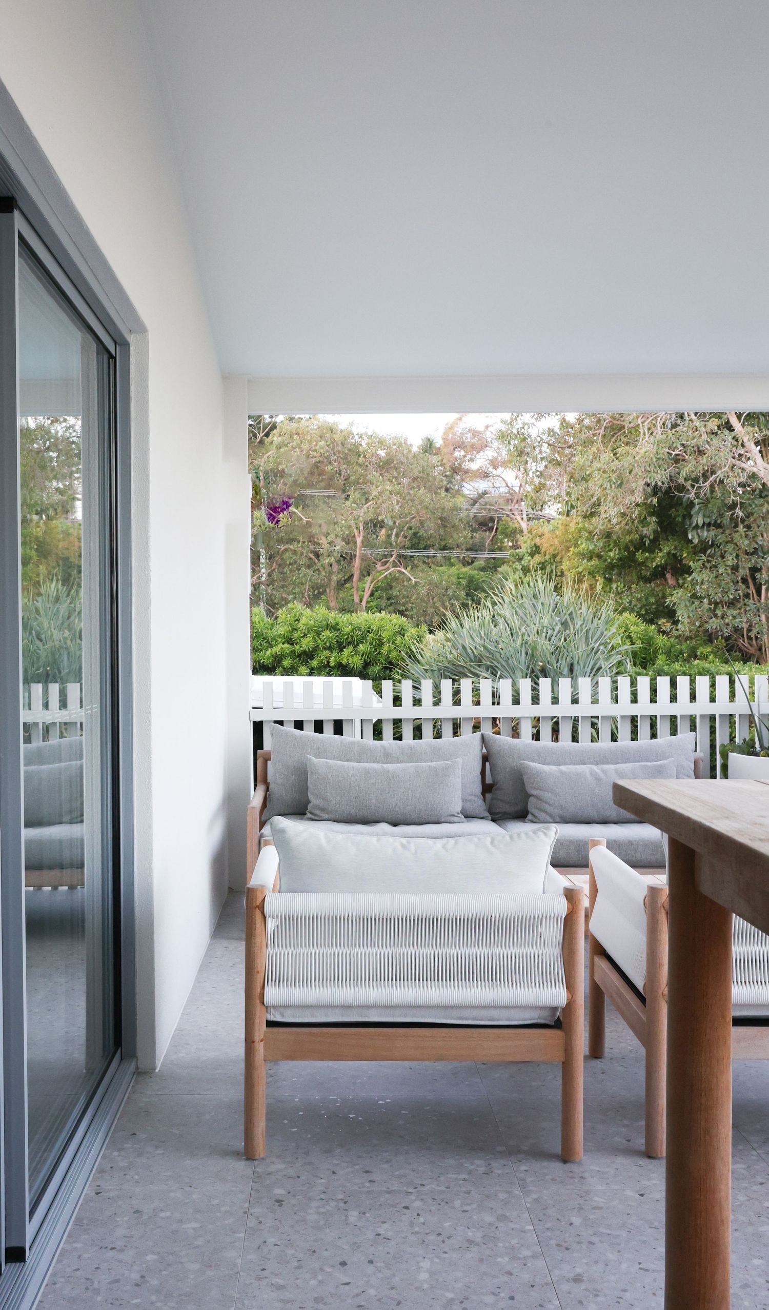 Modern outdoor patio with white cushioned daybed seating and sliding glass doors overlooking a garden space.