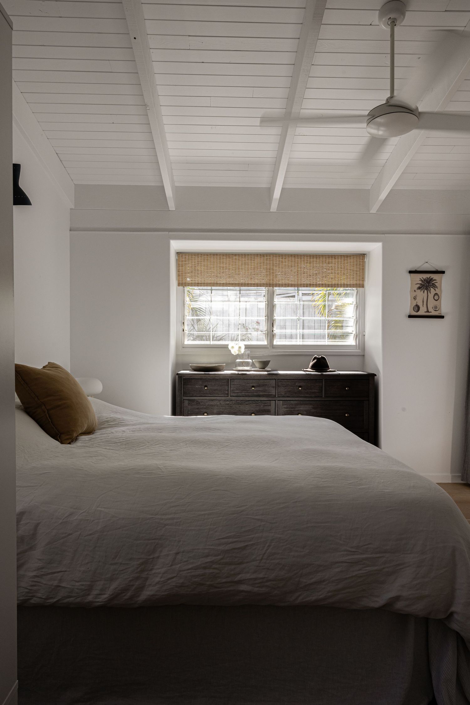 Contemporary bedroom with gray bedding and white plank ceiling features natural woven window shades in a minimalist design.