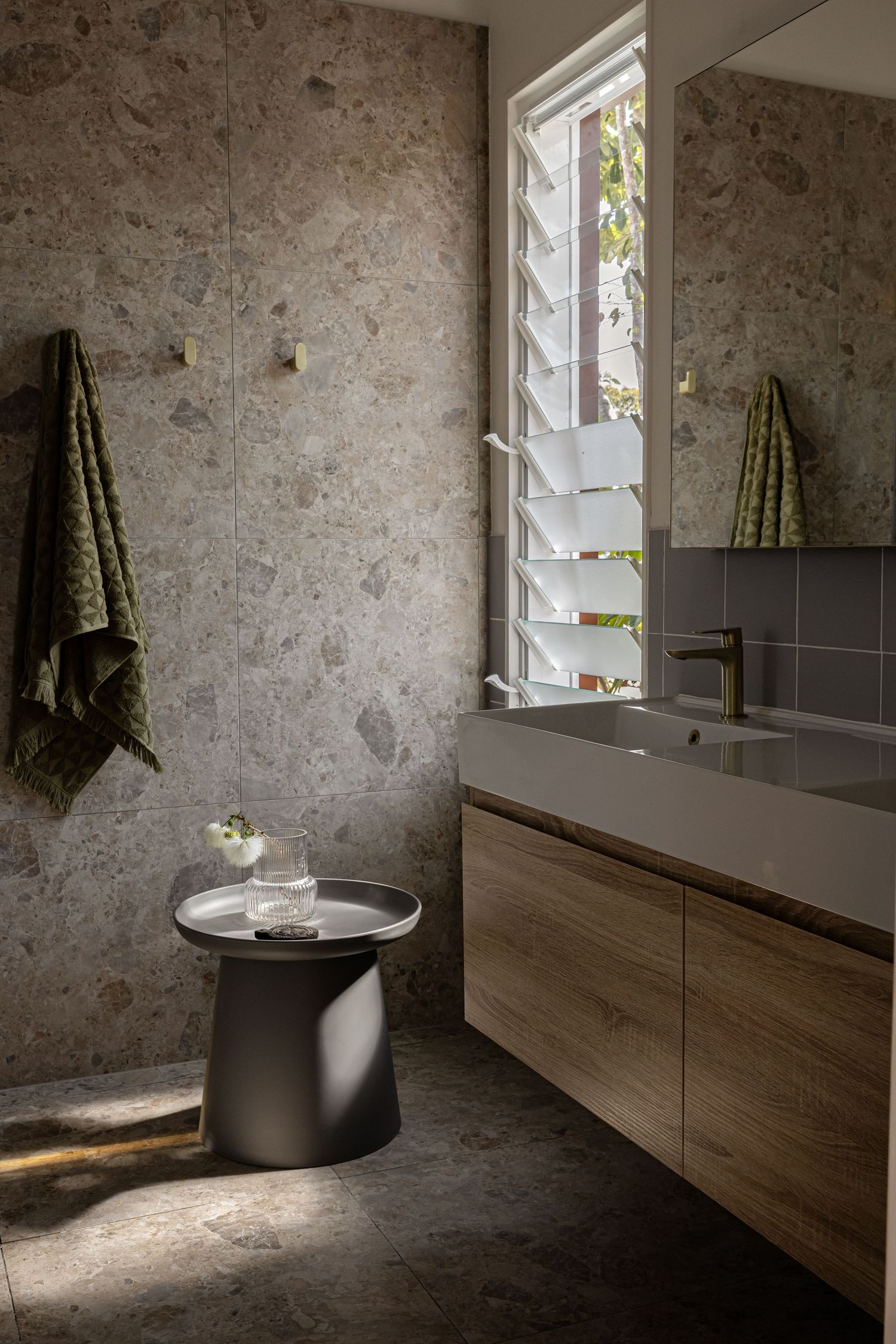 Modern bathroom with wooden vanity, textured walls, and square window letting in natural light.