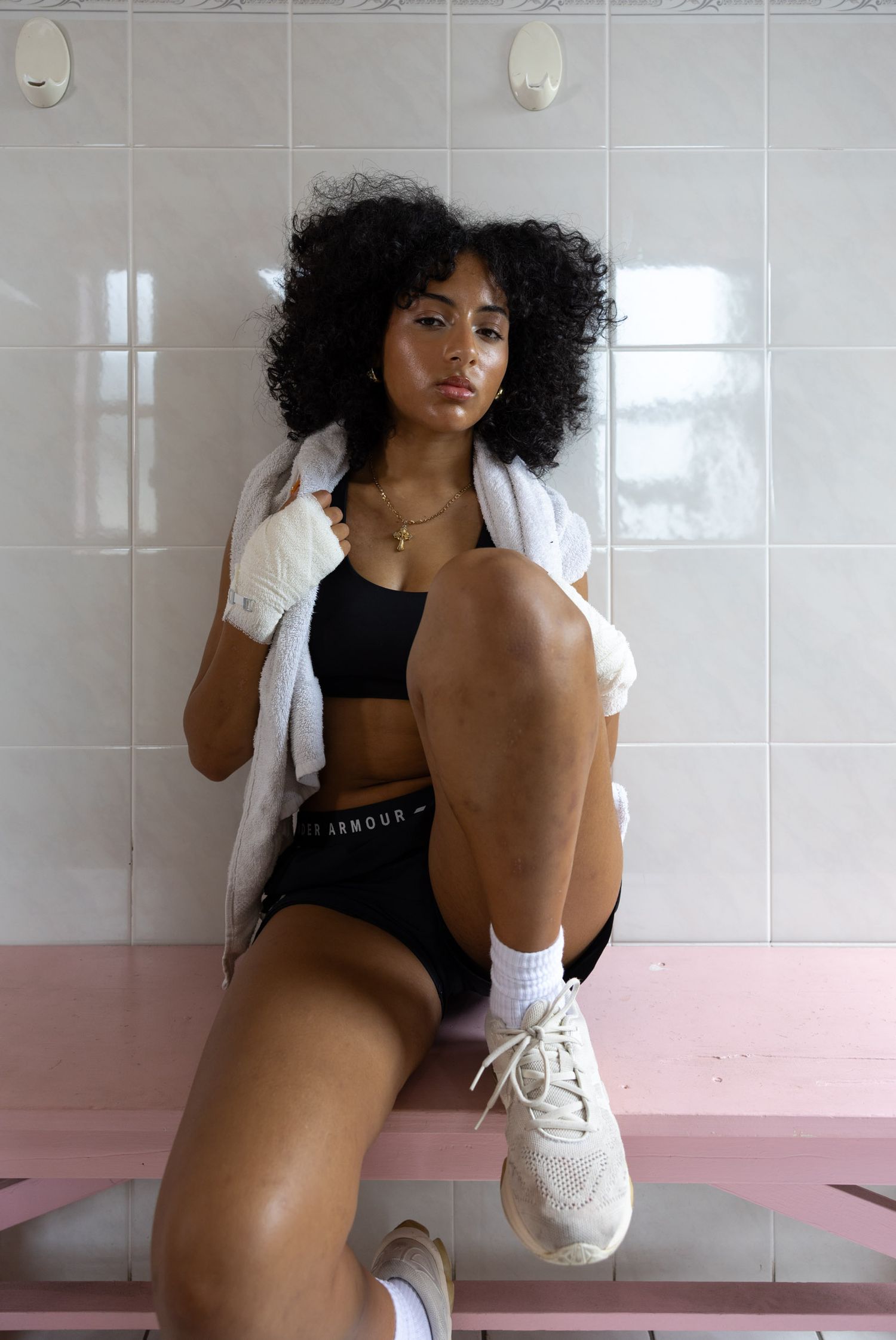 Fitness model in workout clothes and white sneakers posing in tiled bathroom.