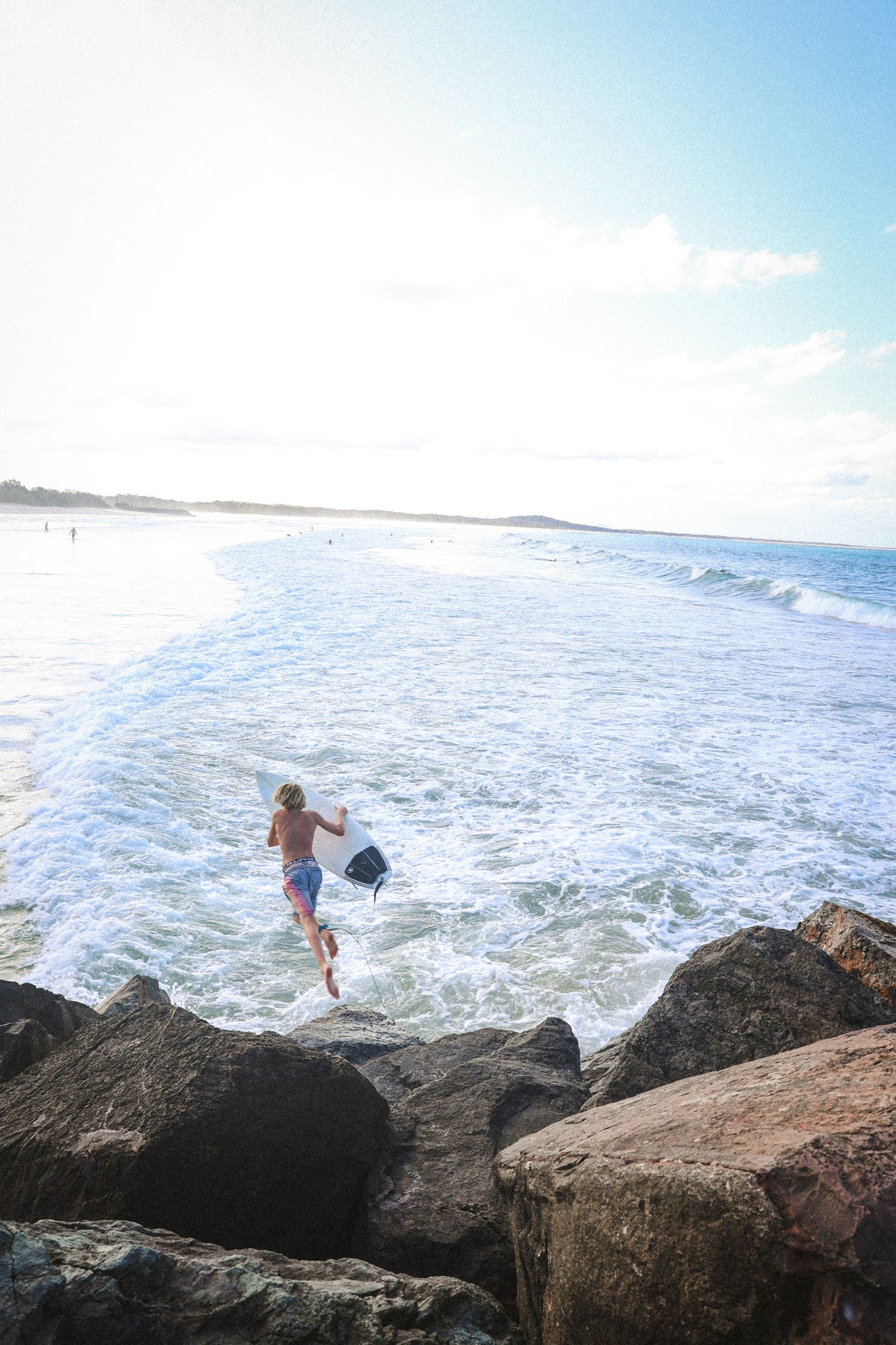 Surfer navigates rocky coastline with crashing waves at a scenic beach.