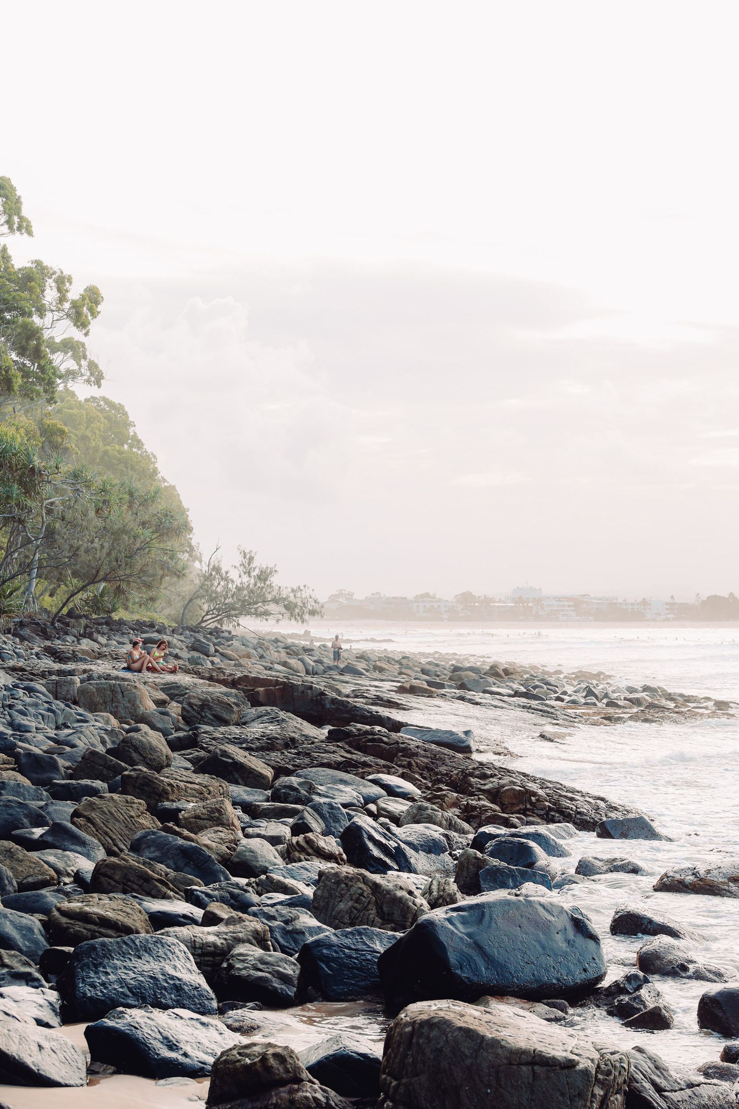 Rocky coastline with large boulders and gentle waves meeting the shore under an overcast sky.