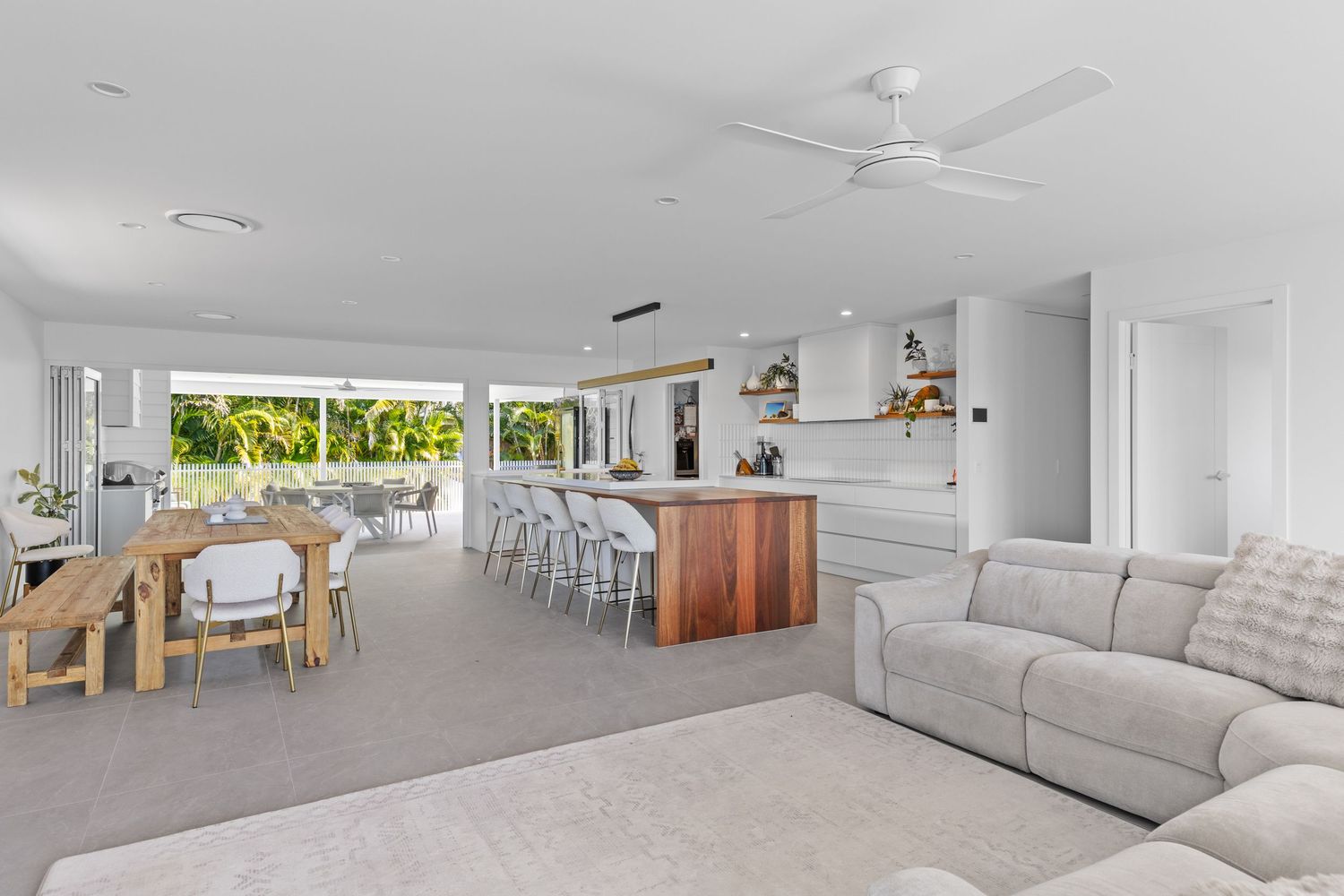 A white contemporary living room displays a minimalist design with ceiling fans and comfortable gray seating.