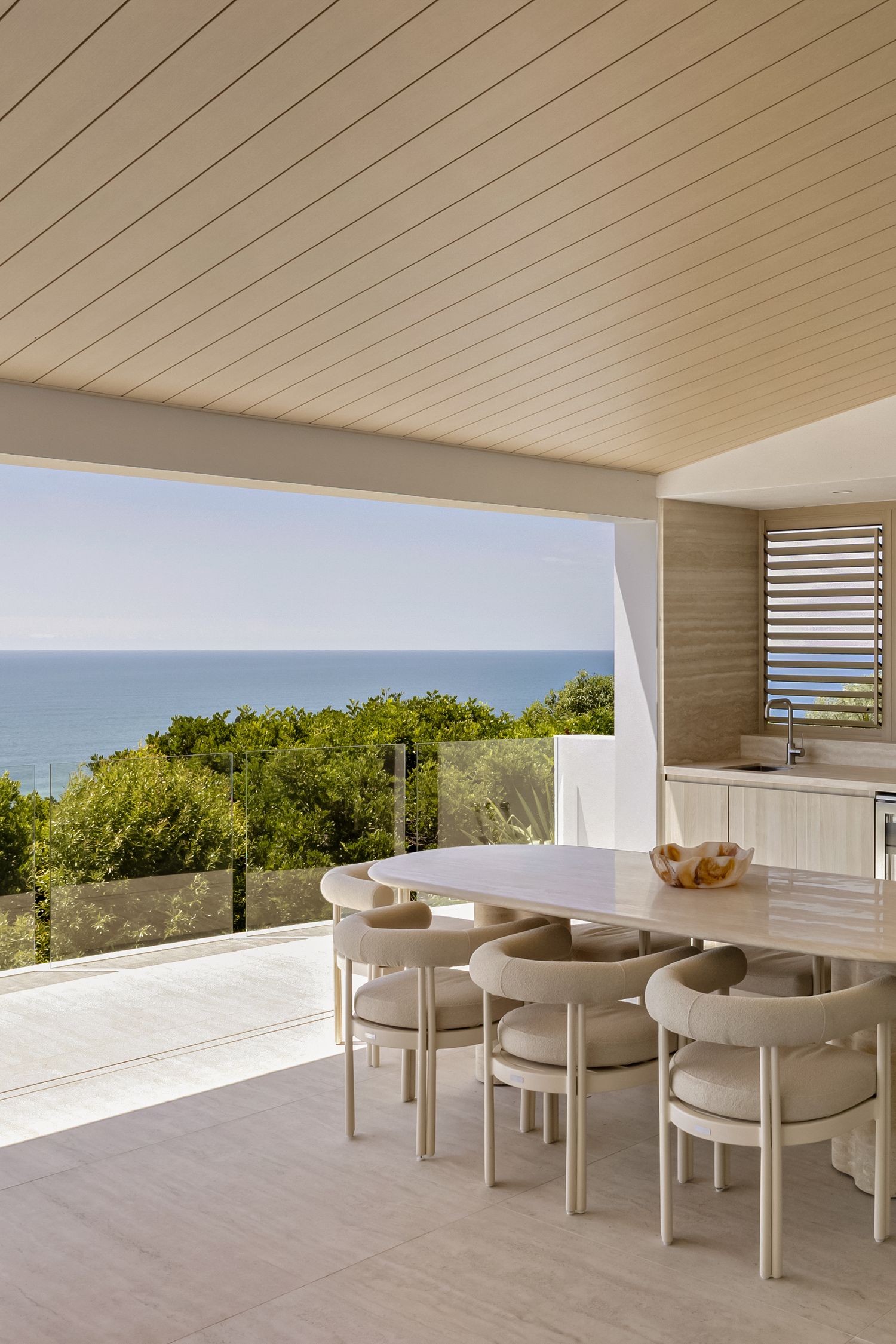 Elegant open-plan dining area with neutral tones, modern chairs, and stunning ocean views through floor-to-ceiling glass panels.
