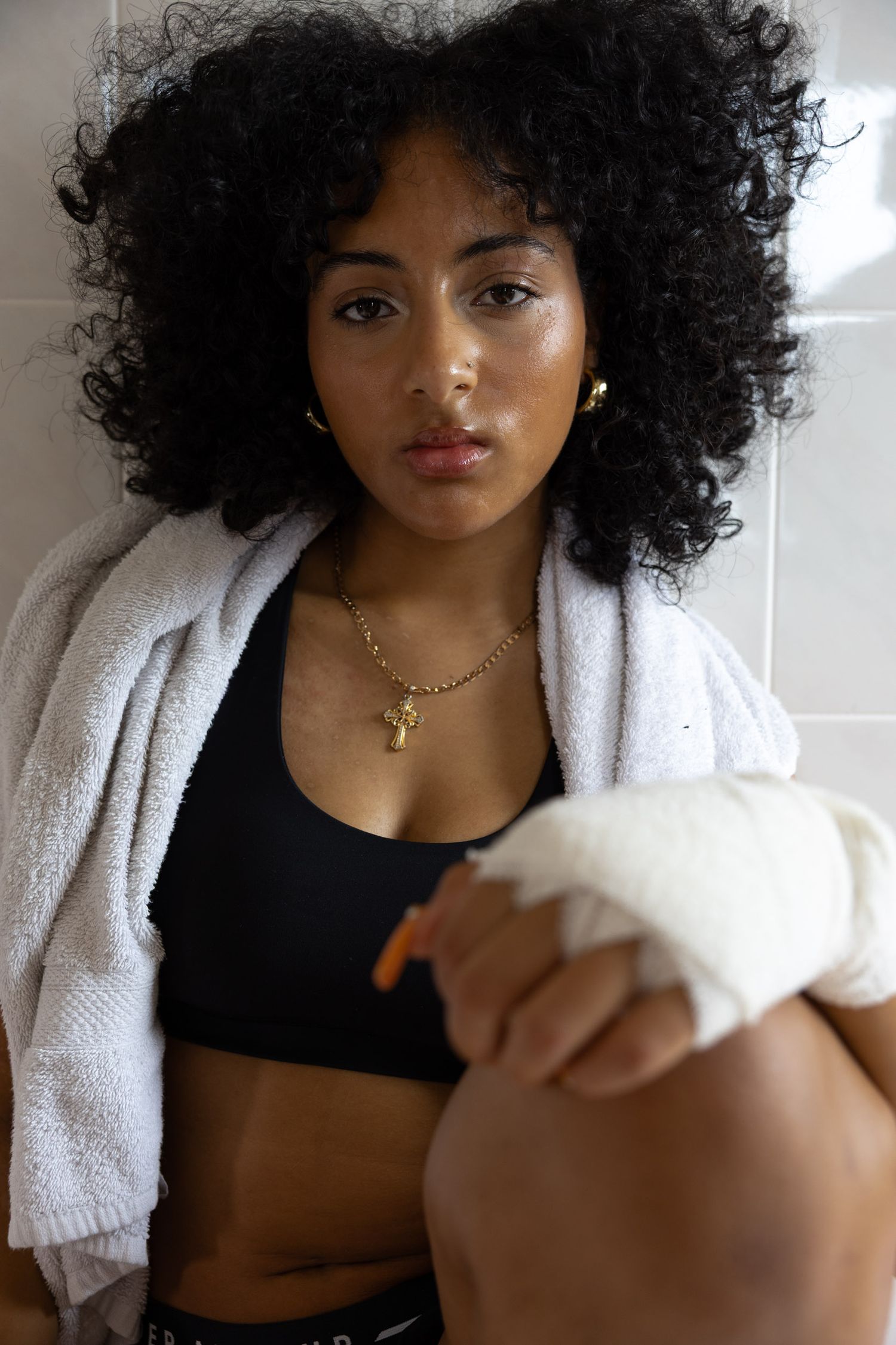 Woman in athletic wear with curly hair posing in bright bathroom setting.