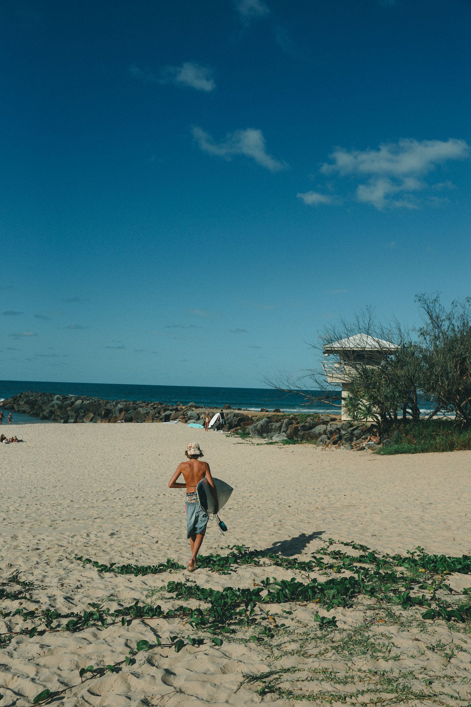 Sandy beach landscape with distant figure walking near coastal rocks.