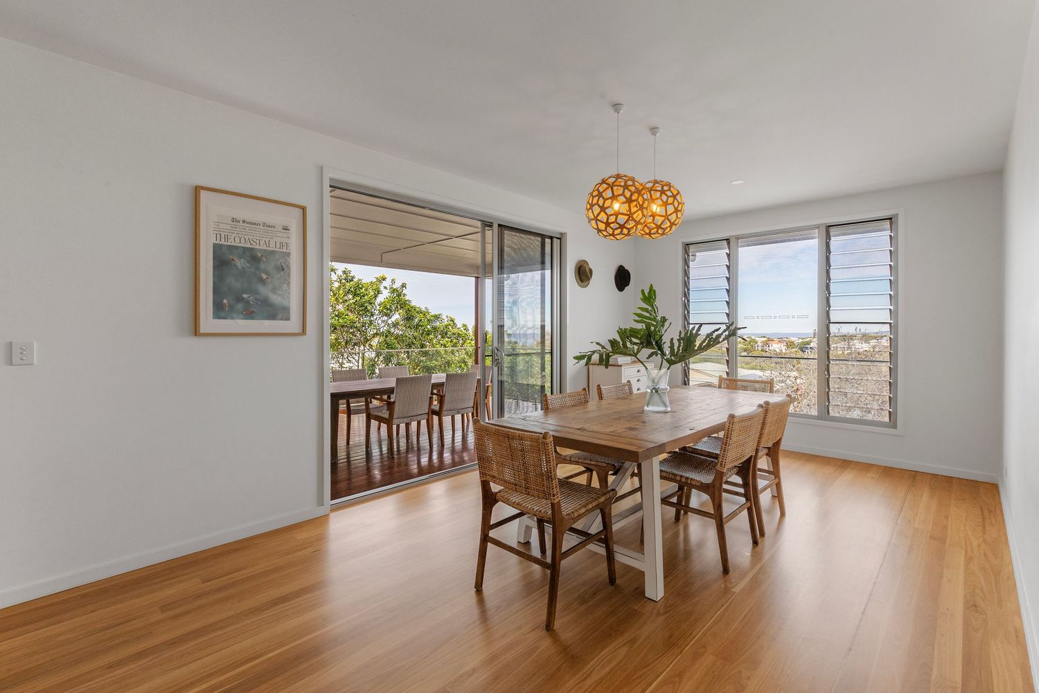 Modern dining room with wooden floors, sliding glass doors to balcony, and orange pendant light fixture above dining set.