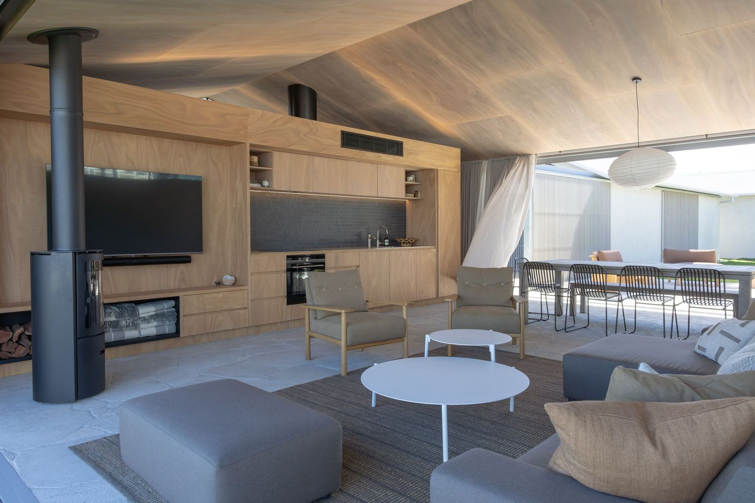 Modern open-concept living area with wood paneling, grey furniture, and black wood stove.