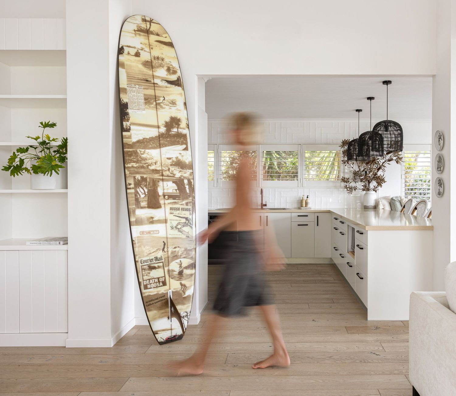 Modern beach house interior featuring a decorative surfboard mirror and white kitchen.