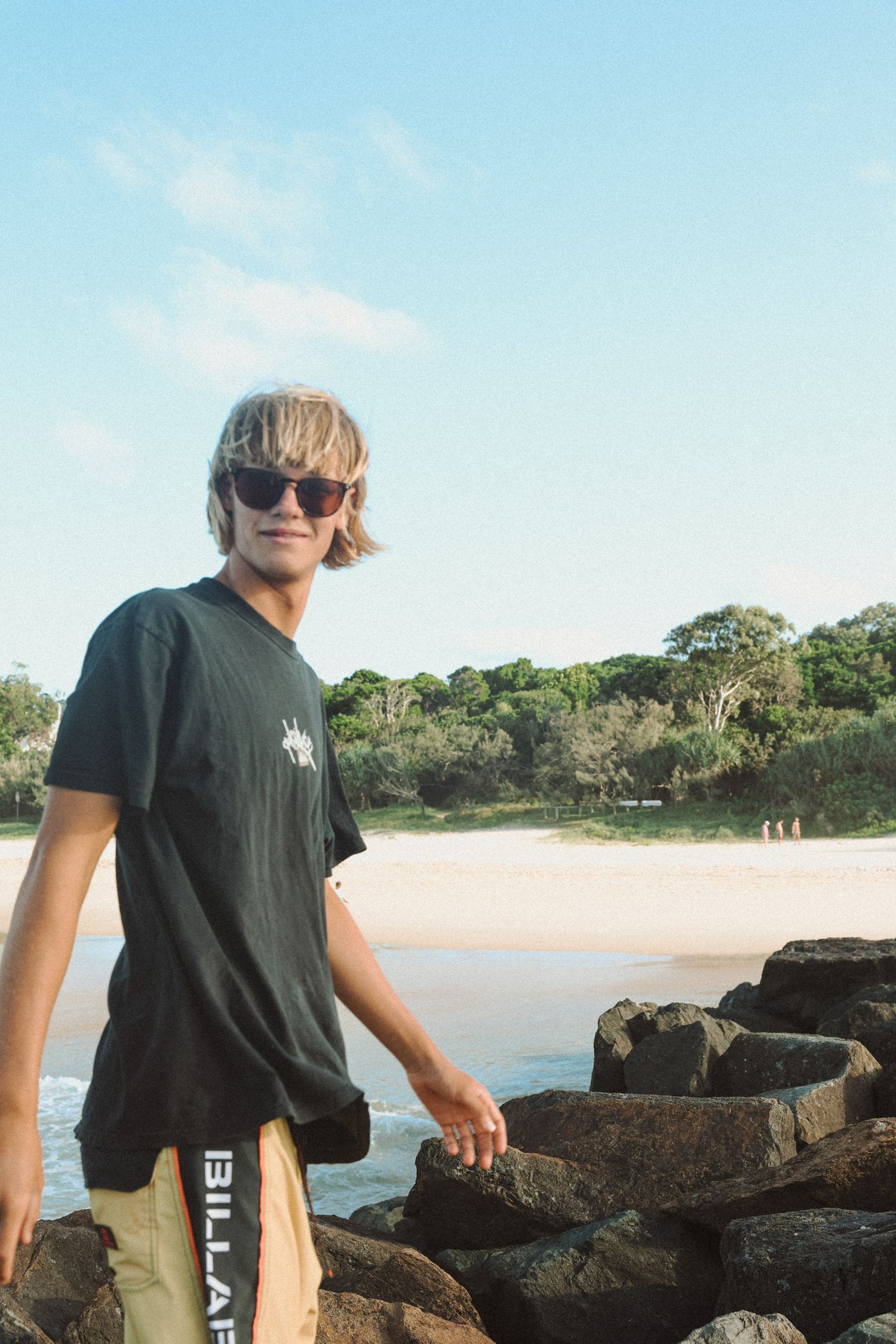 Person on rocky coastal formation wearing casual attire with beach in background.