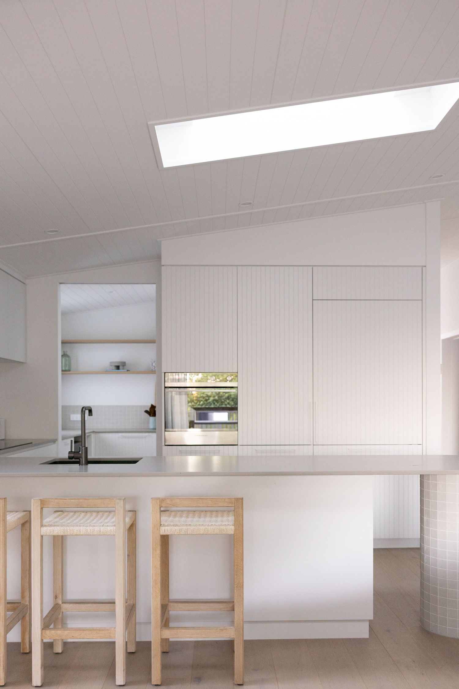 A modern minimalist kitchen features clean white cabinets and light wooden tables in a bright, open space.