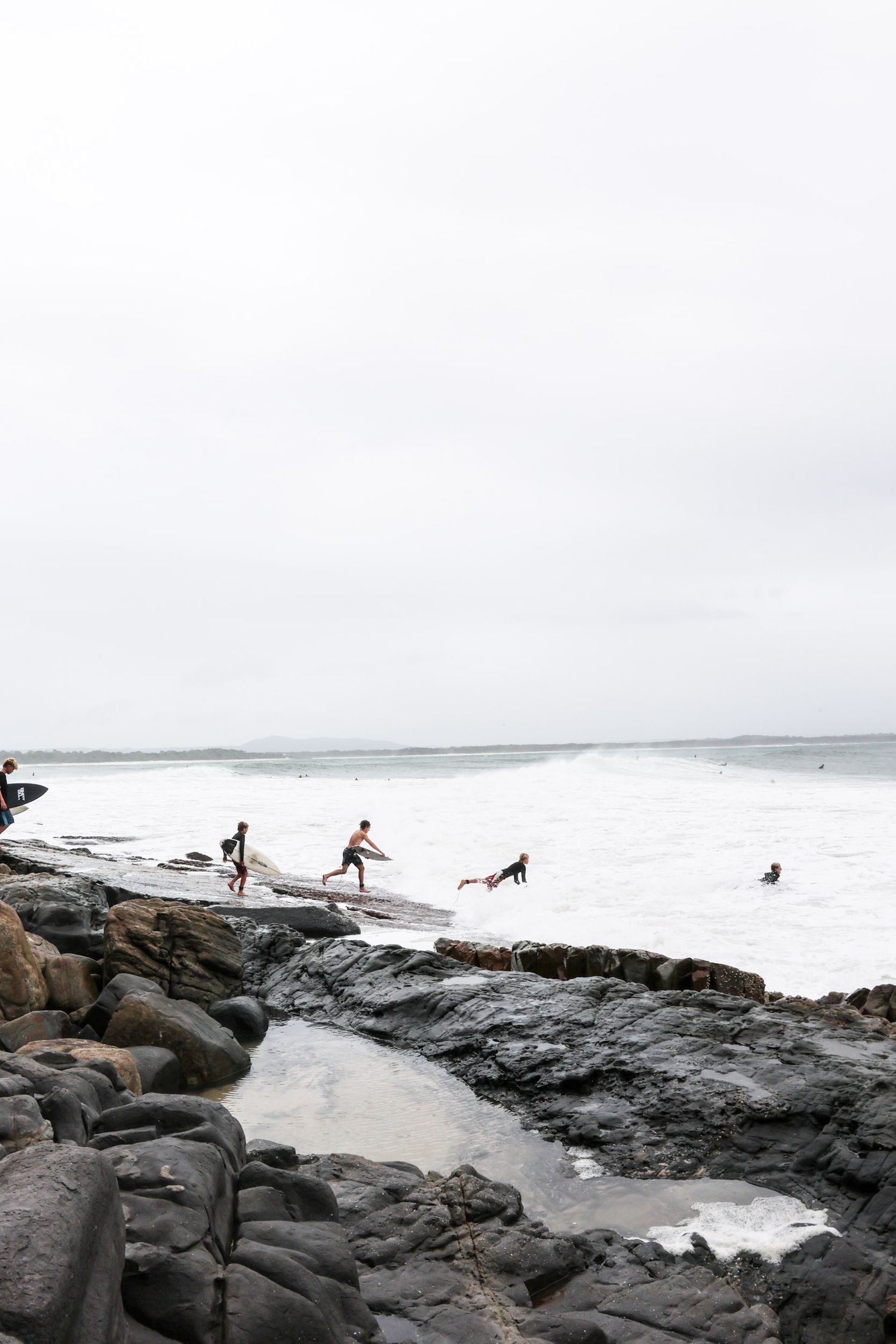 Group navigates rocky coastal outcrop with dog while waves crash below.