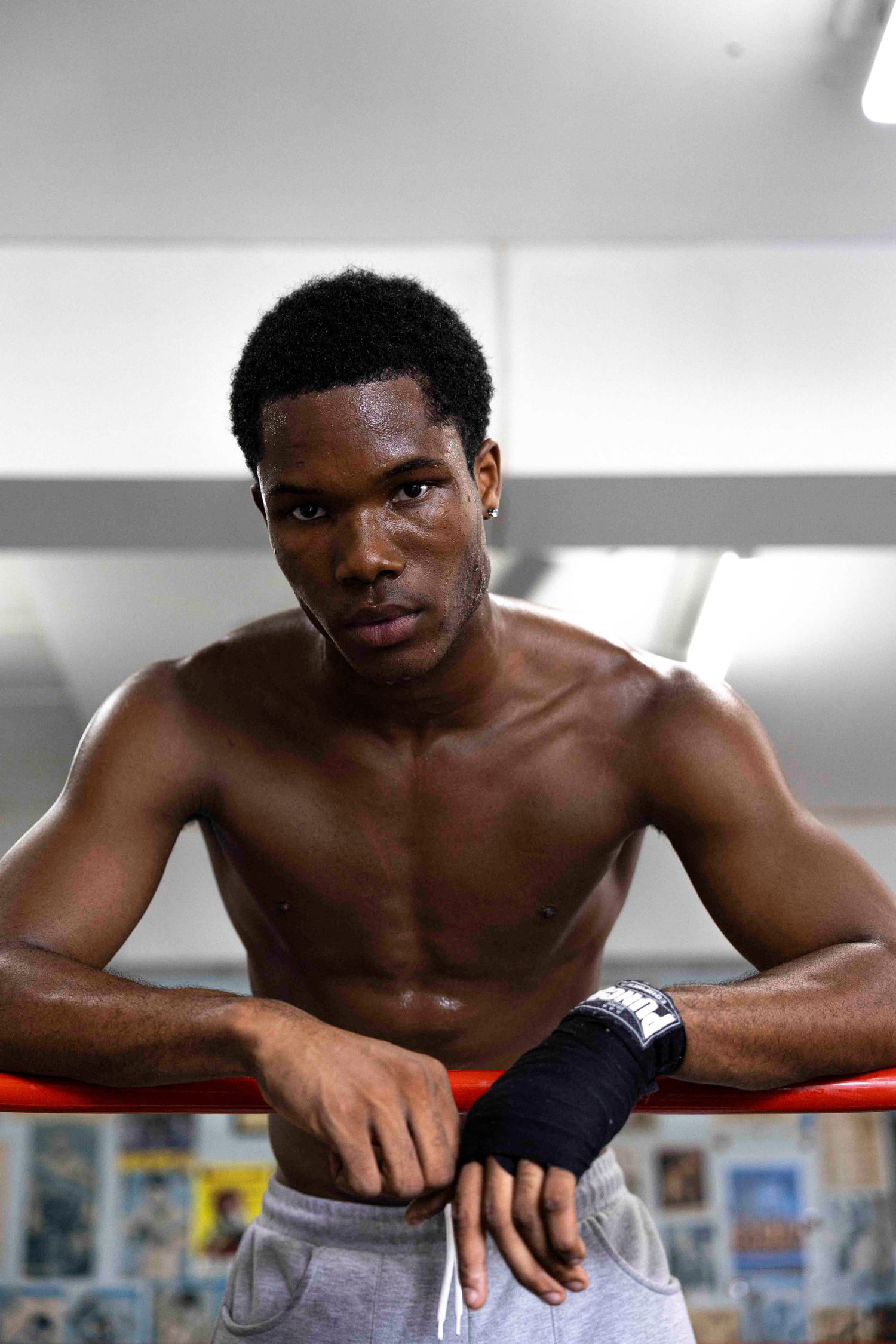 Athletic boxer rests against ropes in training facility.