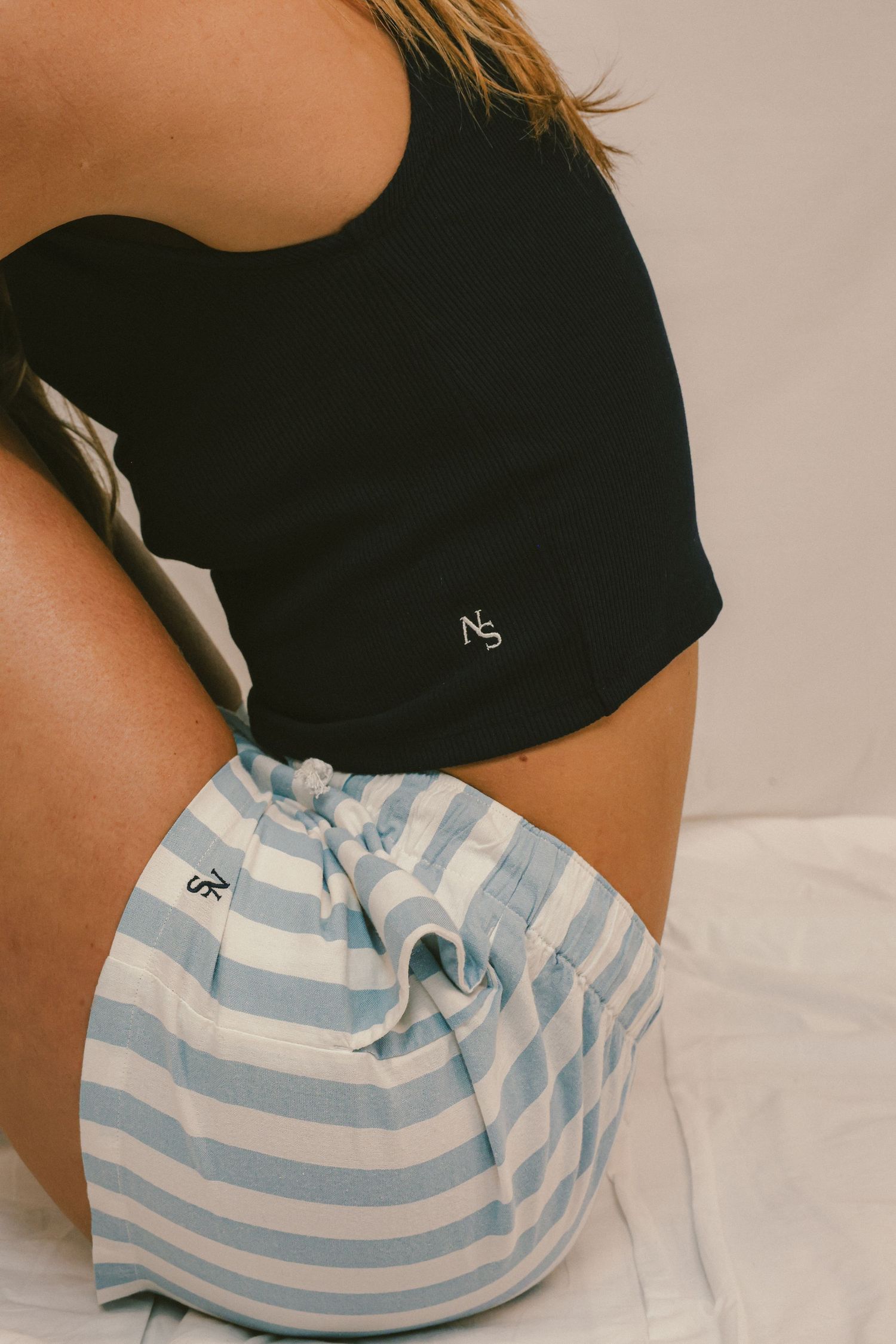 Person lounges on white bedding wearing a black t-shirt and light blue striped shorts in a casual setting.