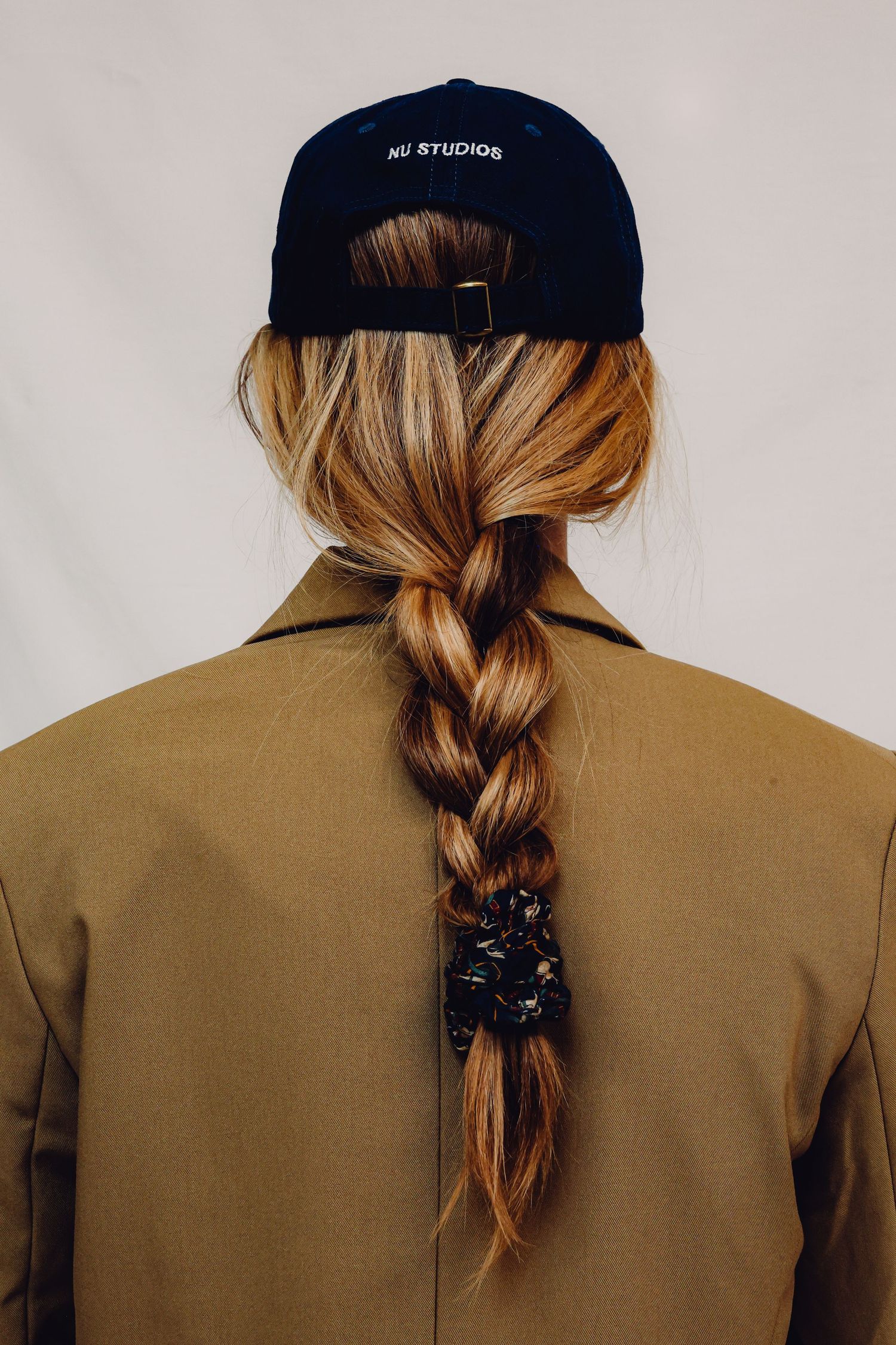 Images show progression of twisting brown hair into a rope braid hairstyle under a black baseball cap, viewed from behind.
