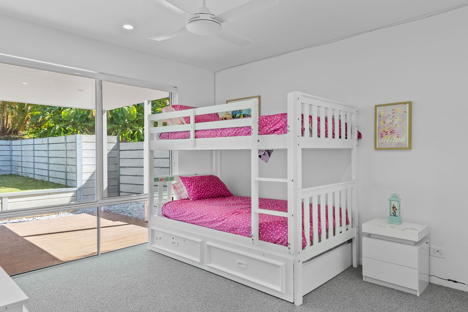 White bunk bed with hot pink bedding in a bright bedroom features built-in storage drawers and safety railings.