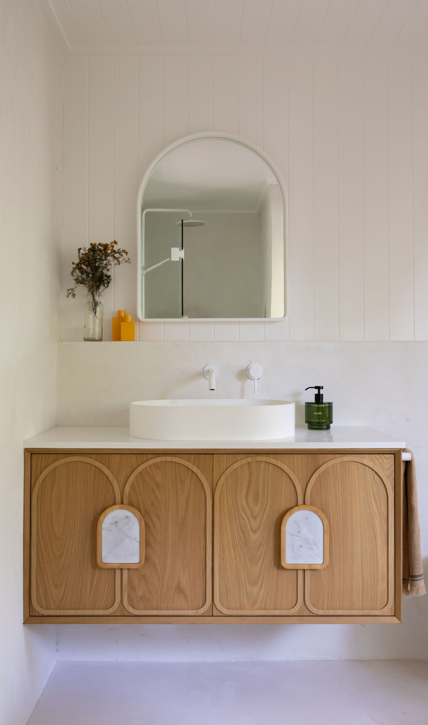 Modern bathroom vanity with arched mirror features wooden cabinet doors with decorative arch details and white vessel sink.