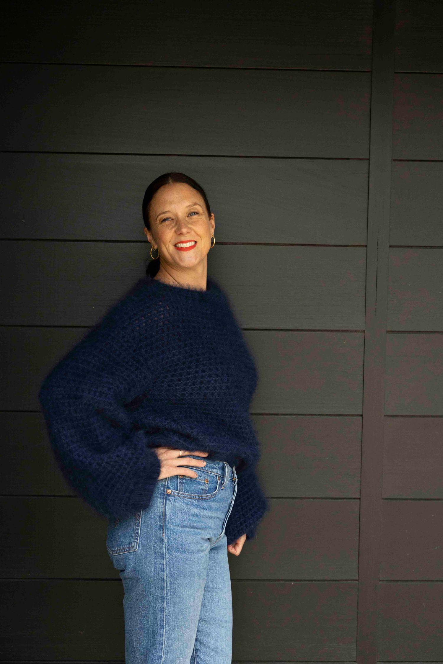 Person wearing cozy navy sweater and jeans poses against dark wall.