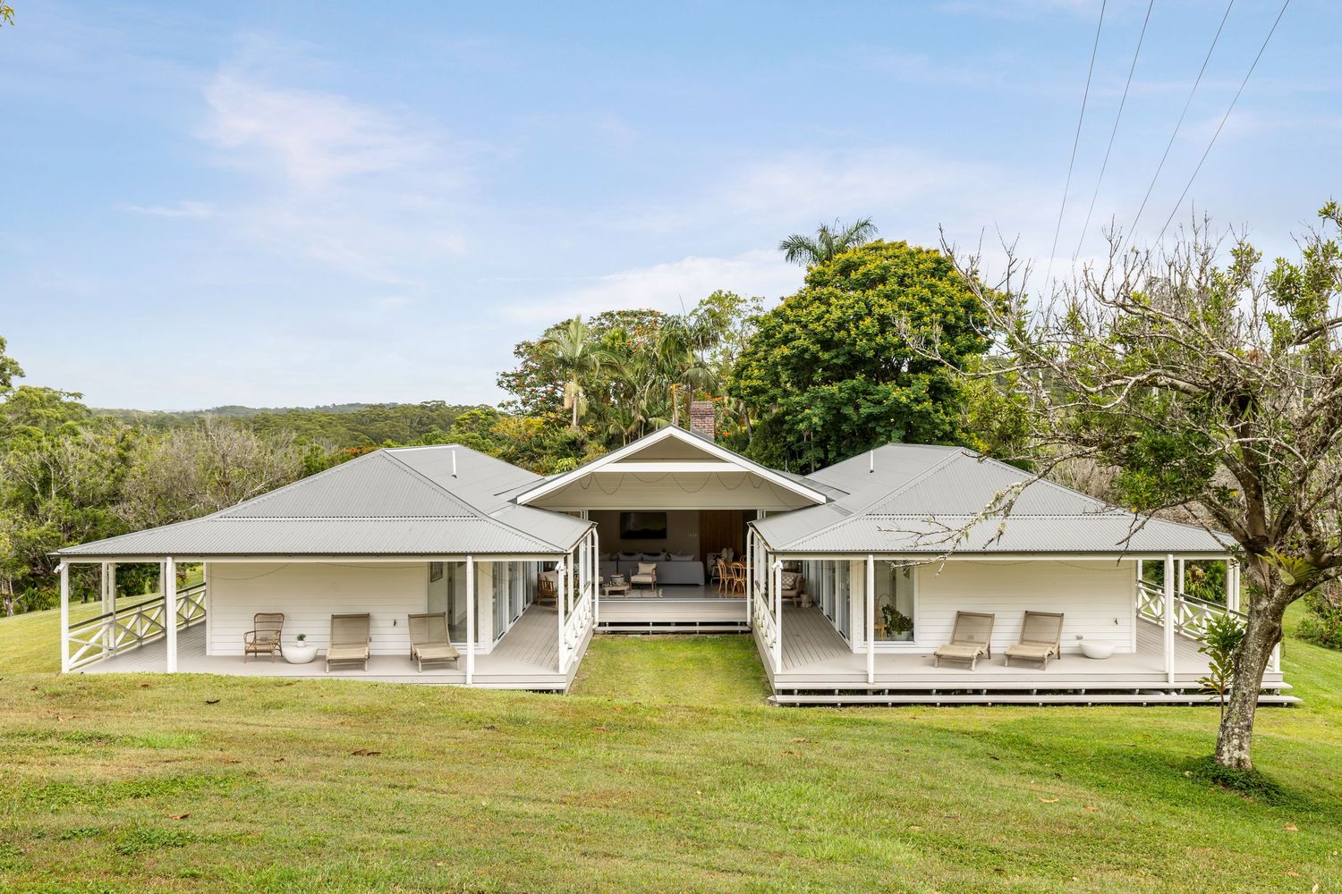 Modern white ranch-style house with twin wings and covered porch set on green lawn with trees in rural setting.