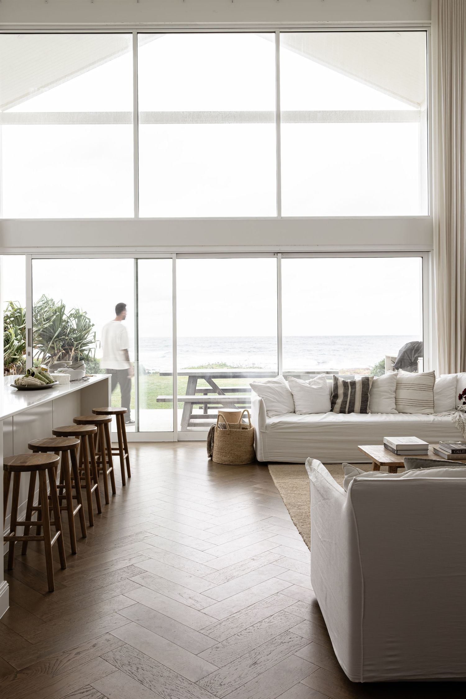 Modern white living room interior with herringbone wood floors and large windows offering panoramic views.