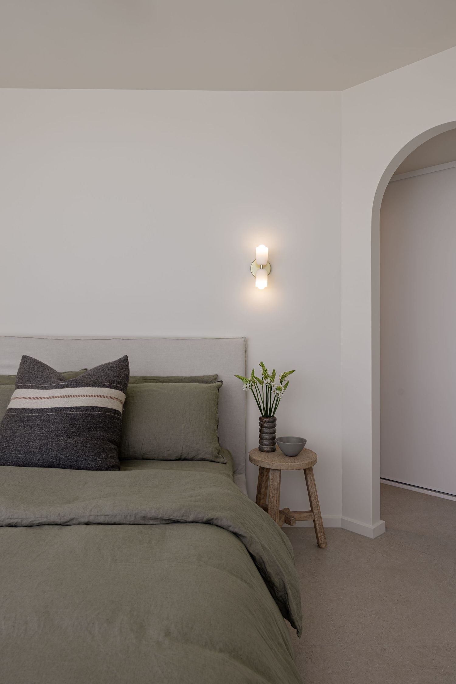 A series of minimalist bedroom views showing gray bedding and white walls with recessed lighting and small side tables.