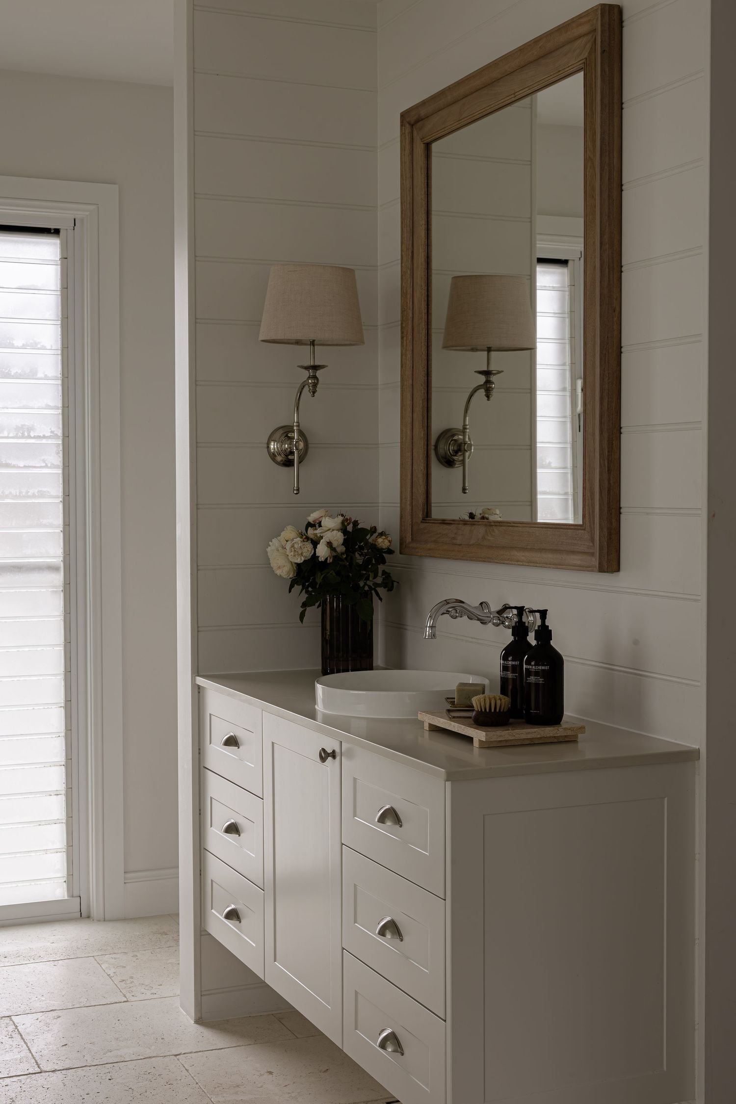Modern white bathroom vanity with wooden framed mirror and black hardware creates a sleek, coastal farmhouse design.