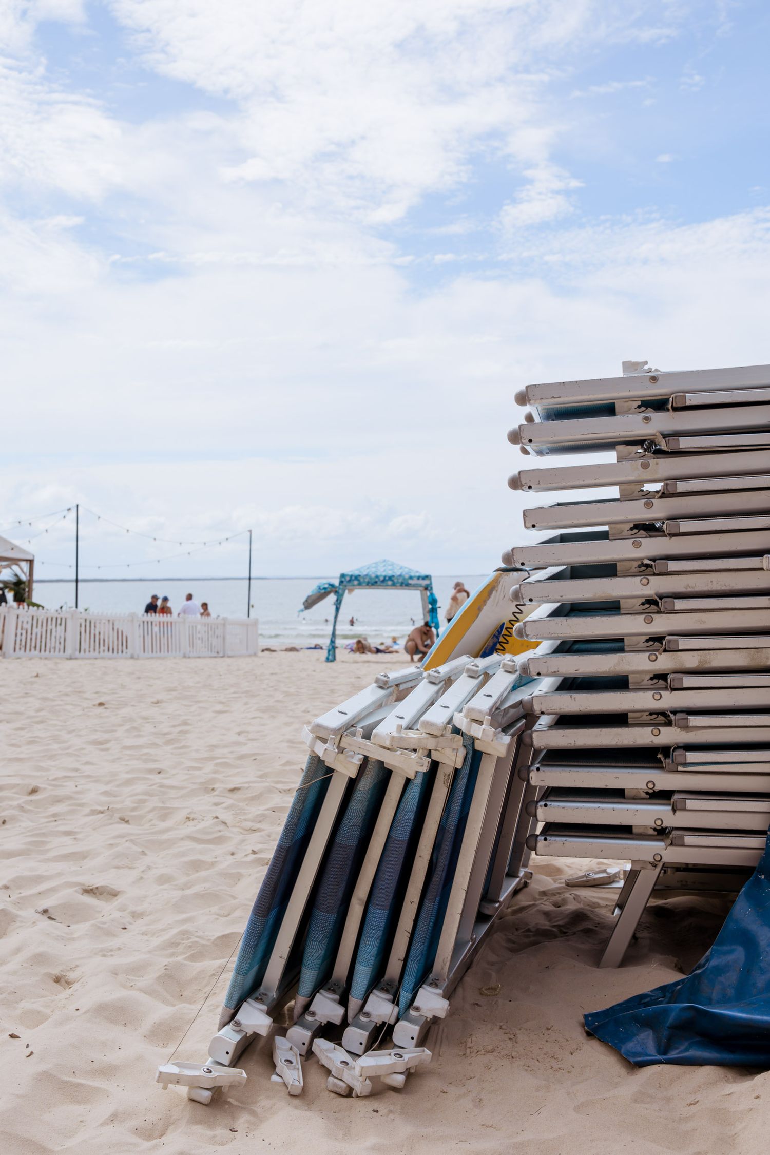 Stack of beach chairs and umbrellas on sandy beach with ocean view.