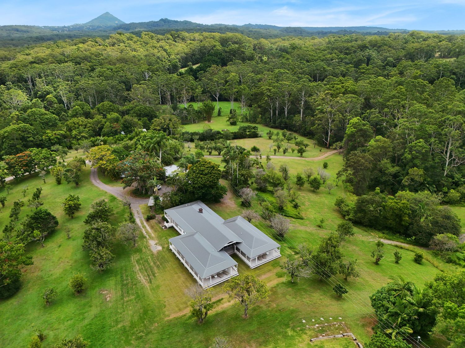 Aerial panorama of a rural property with solar panels, green pastures, and mountains in the distance under blue skies.