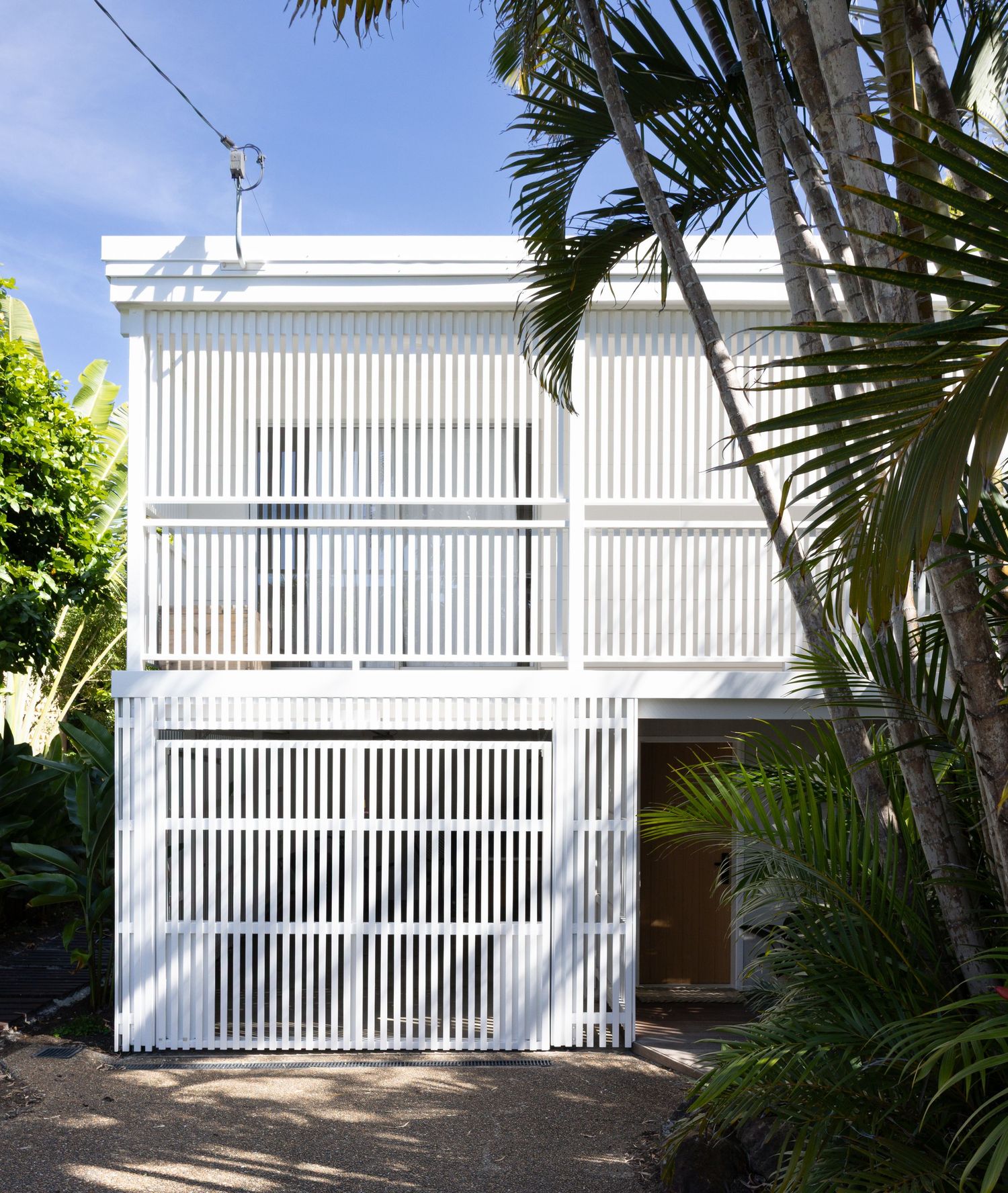 White slatted garage door with tropical palm trees and landscaping creating a modern residential entrance.