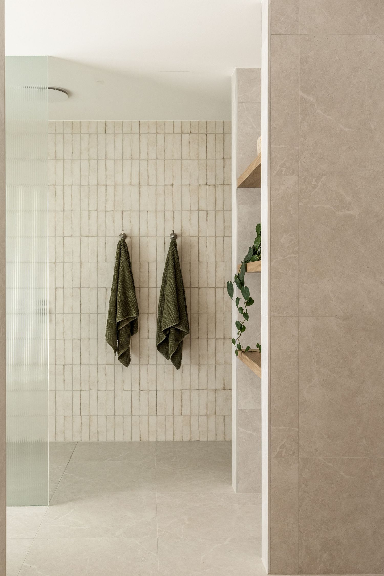Minimalist bathroom interior with vertical white tiles, green towels, and curved architectural elements.