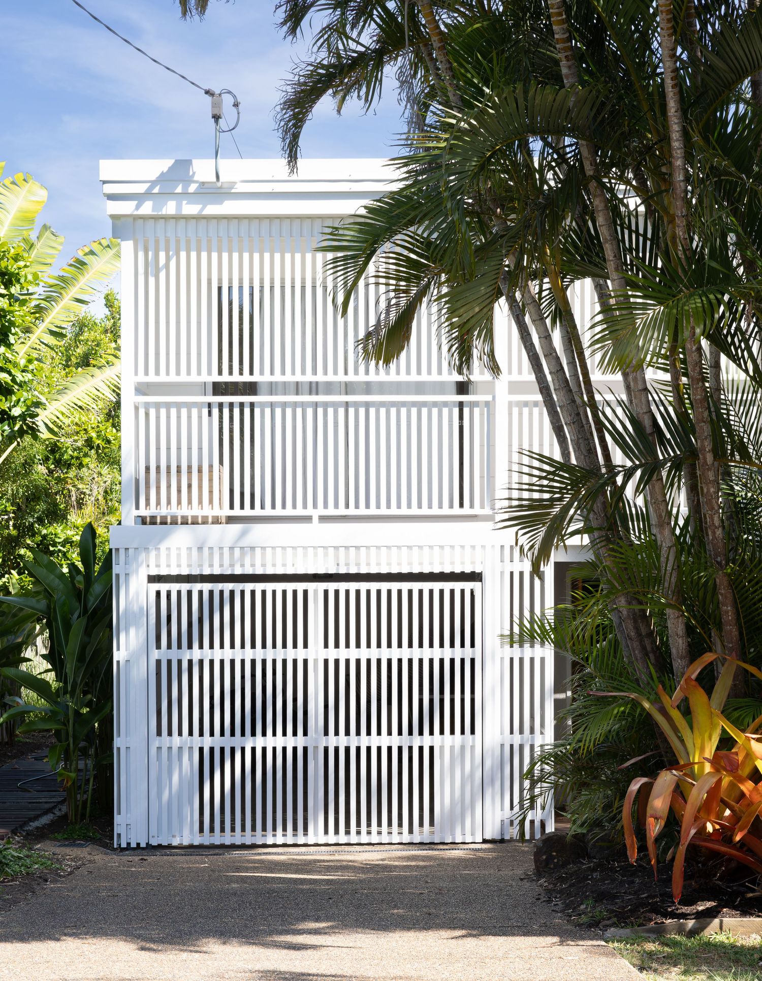 Modern white slatted garage door with tropical palm trees and landscaping framing the entrance.
