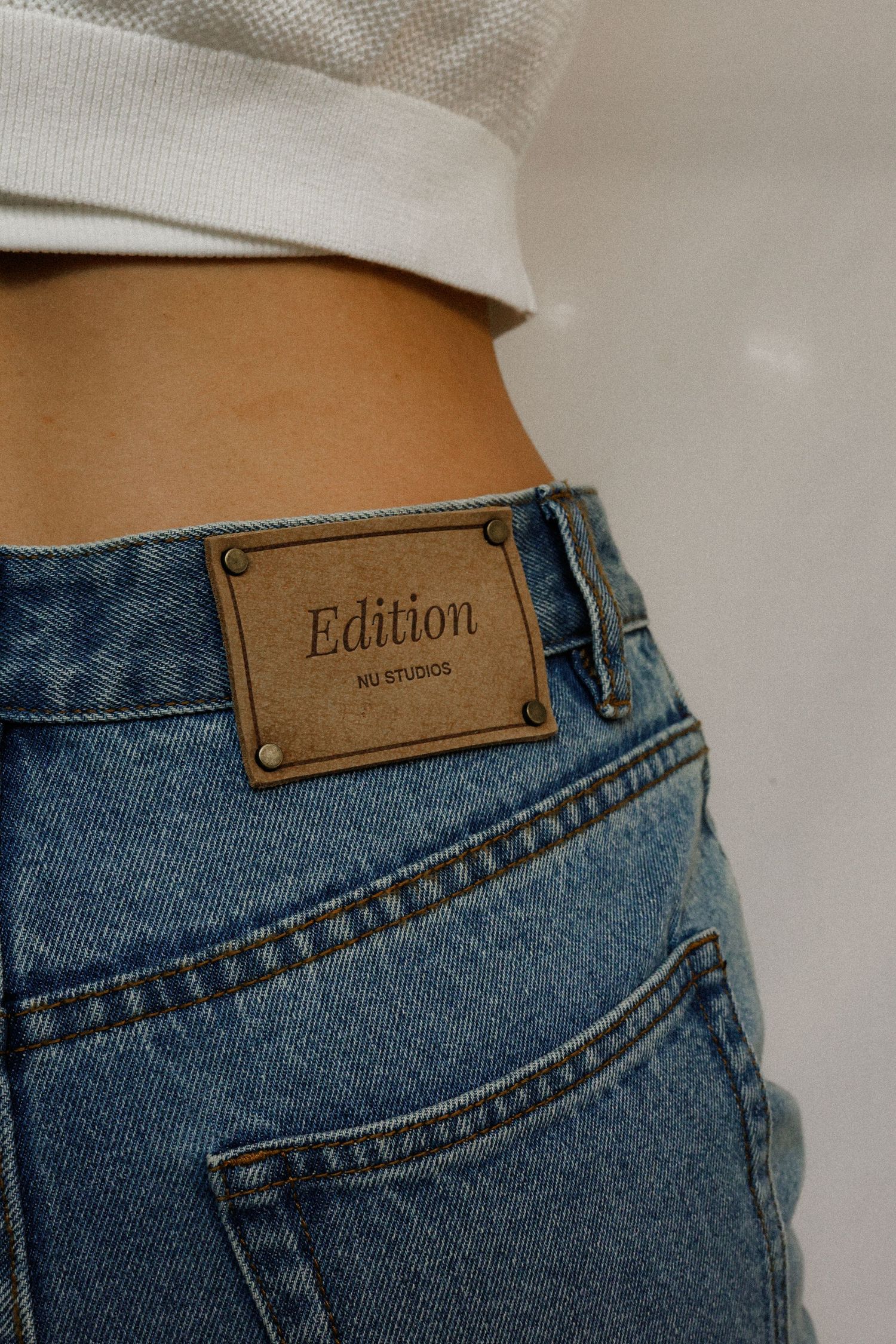 Close-up view of brown leather jean tags showing the word 'Edition' on classic blue denim jeans.
