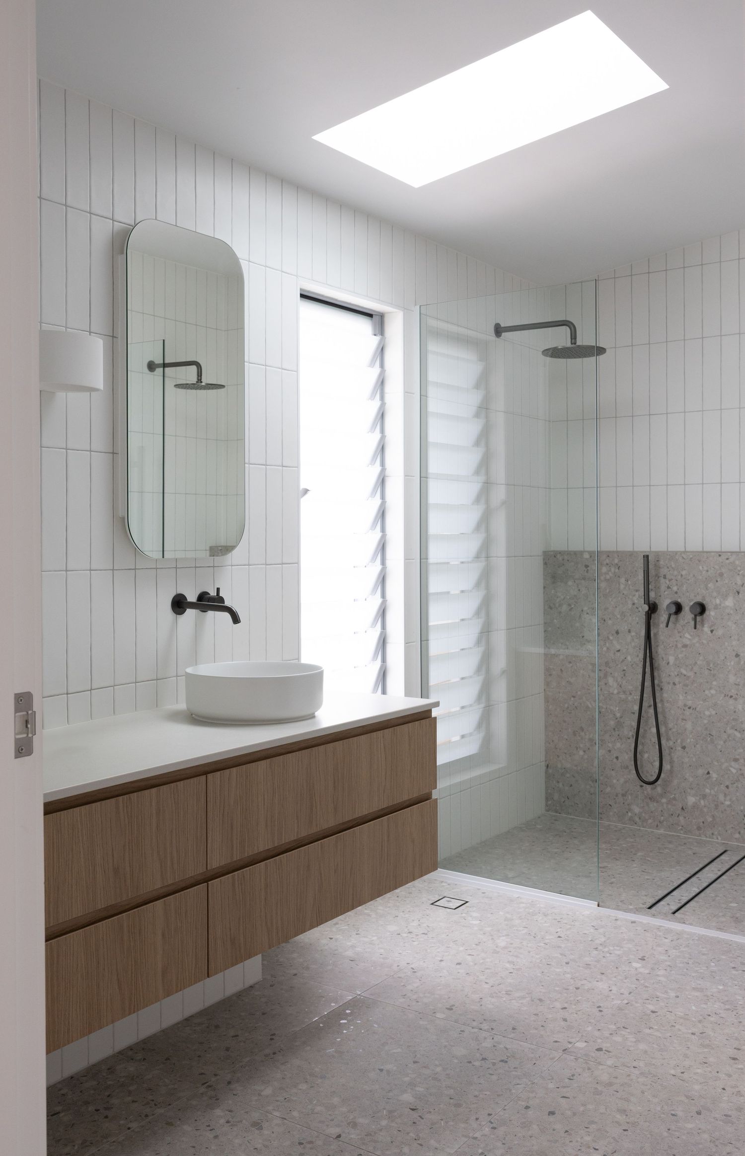 Modern bathroom interior features white tiled walls, wooden vanity cabinets, and natural lighting from skylights and windows.