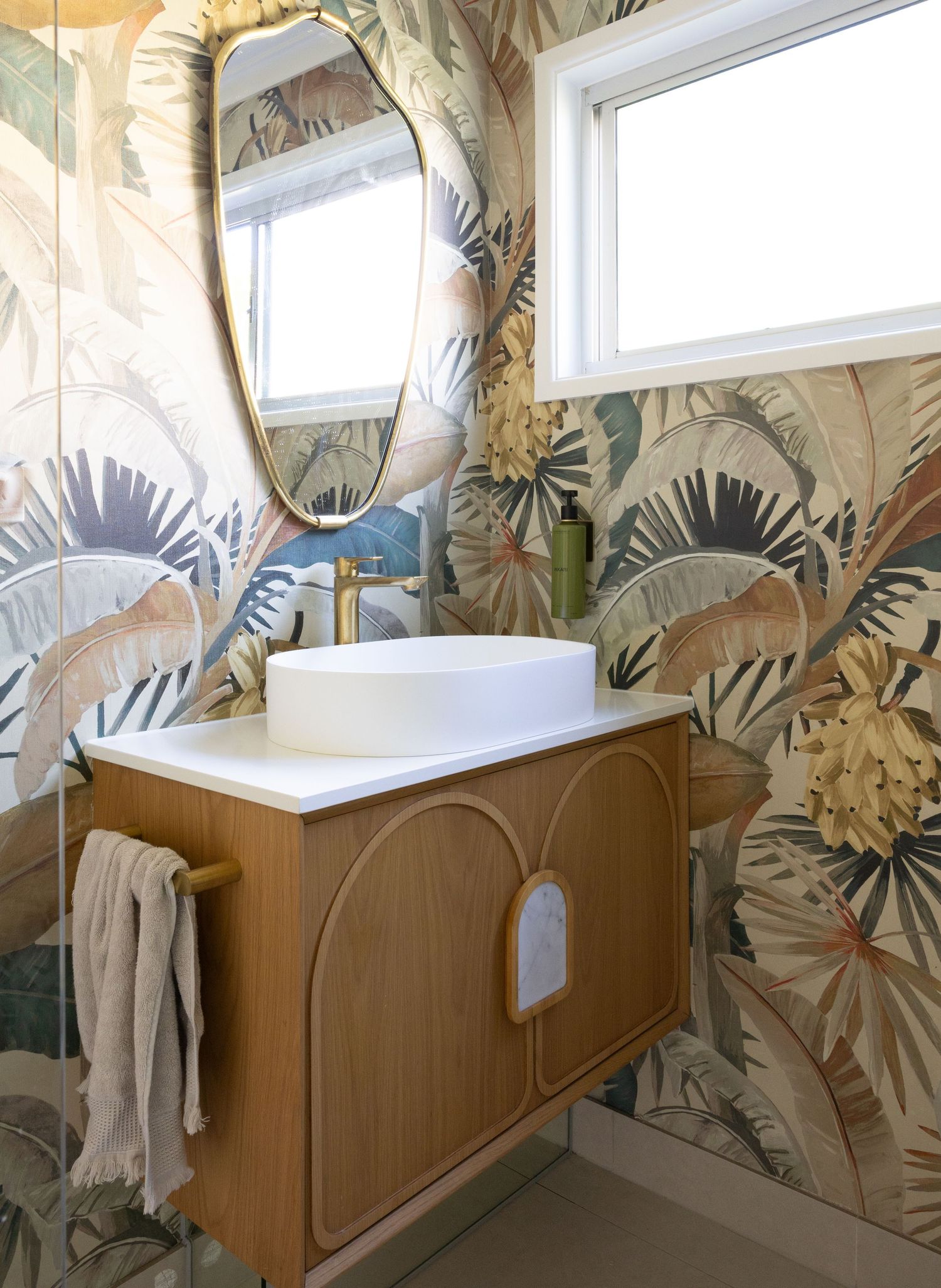 Modern bathroom interior with wooden vanity cabinets and floral wallpaper featuring clerestory windows above.